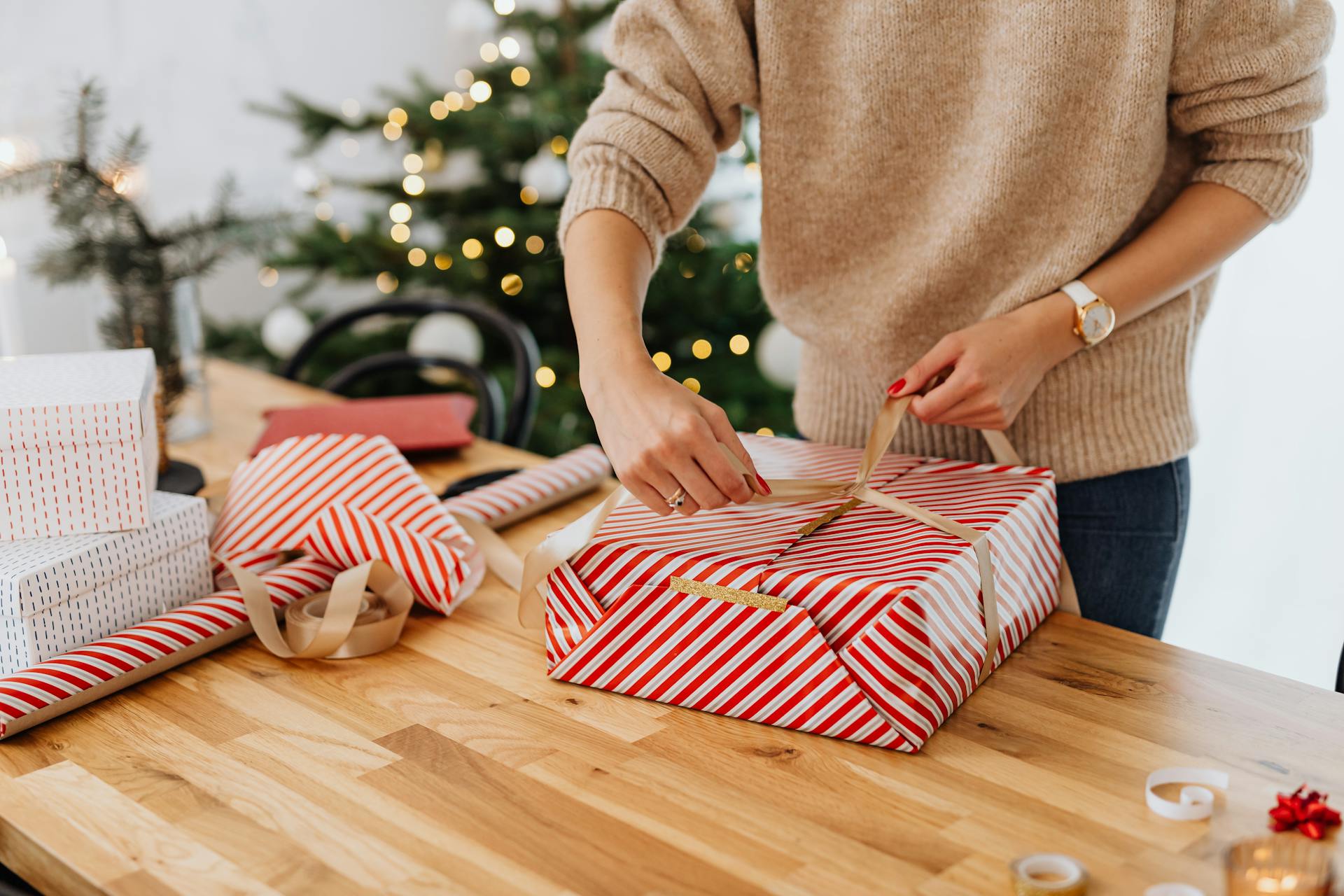 Una mujer envuelve un regalo con un árbol de Navidad de fondo | Fuente: Pexels