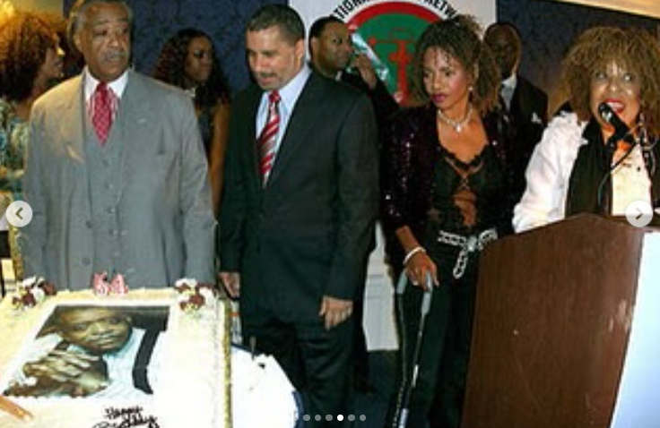 Al Sharpton de pie junto a un pastel de celebración en un acto de homenaje a líderes comunitarios, rodeado de amigos, entre ellos Roberta Flack, publicado el 24 de febrero de 2025. | Fuente: Instagram/real_sharpton