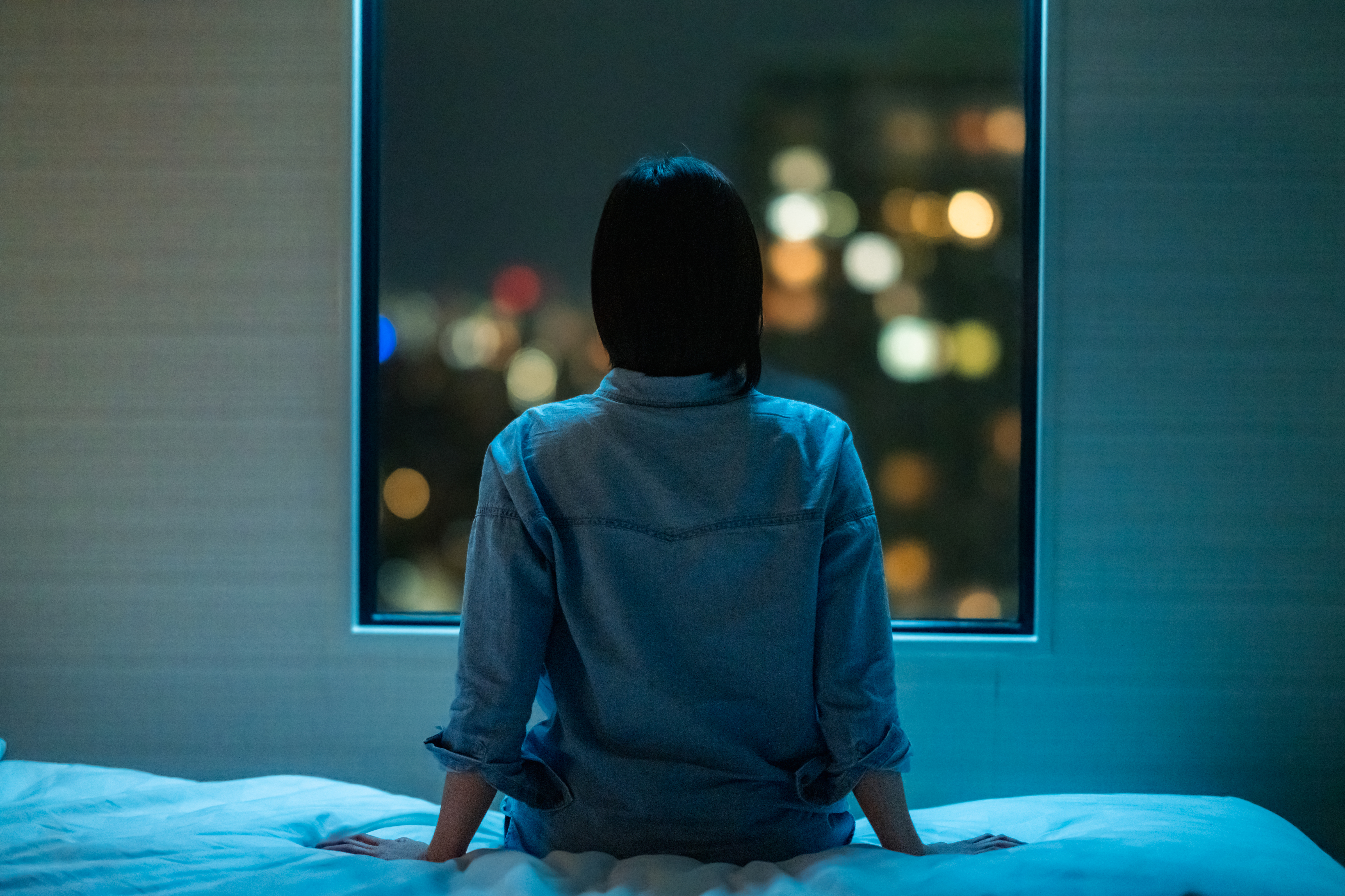 Mujer sentada en la cama mirando por la ventana por la noche | Foto: Getty Images