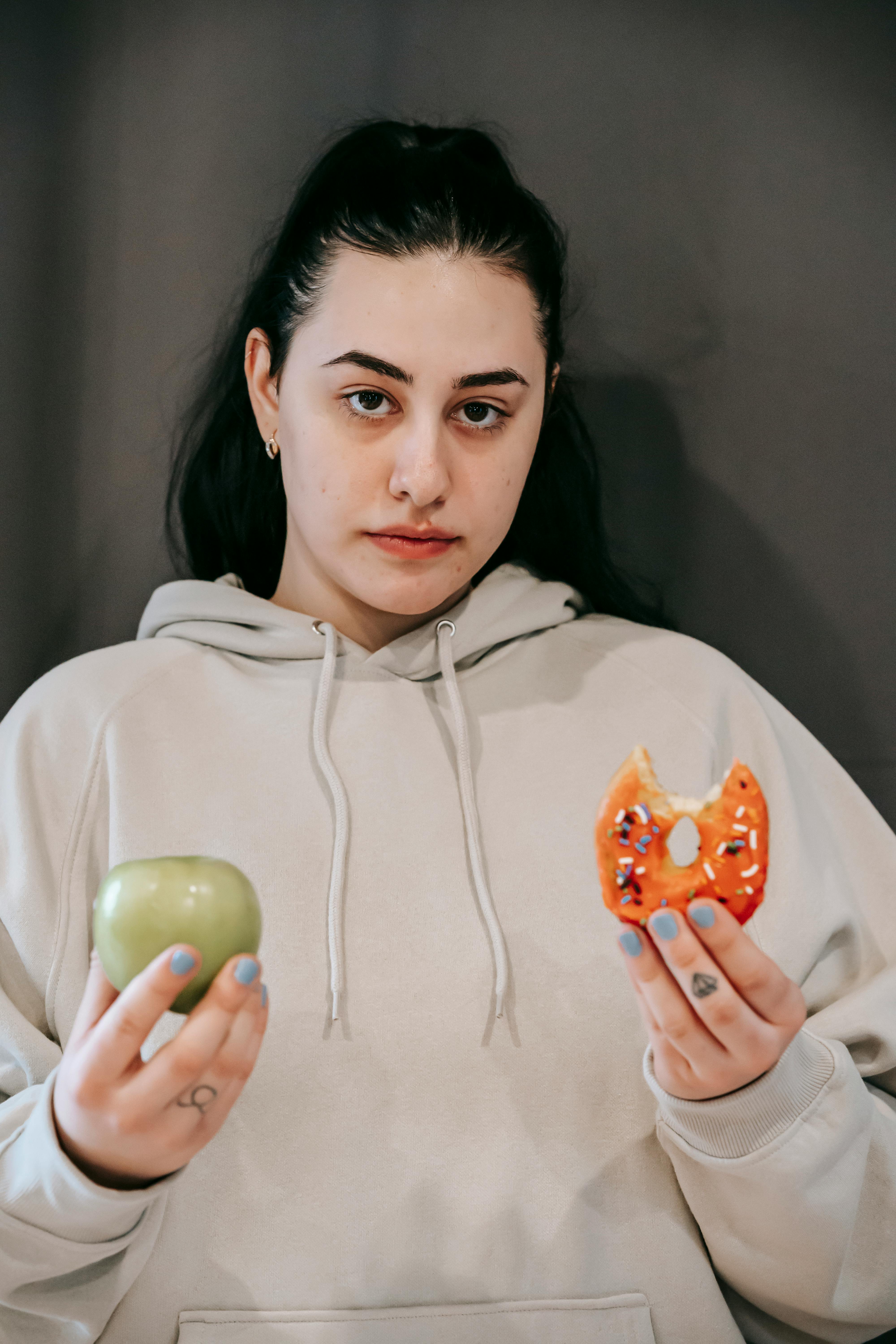 Una mujer con una manzana y un donut en la mano | Fuente: Pexels