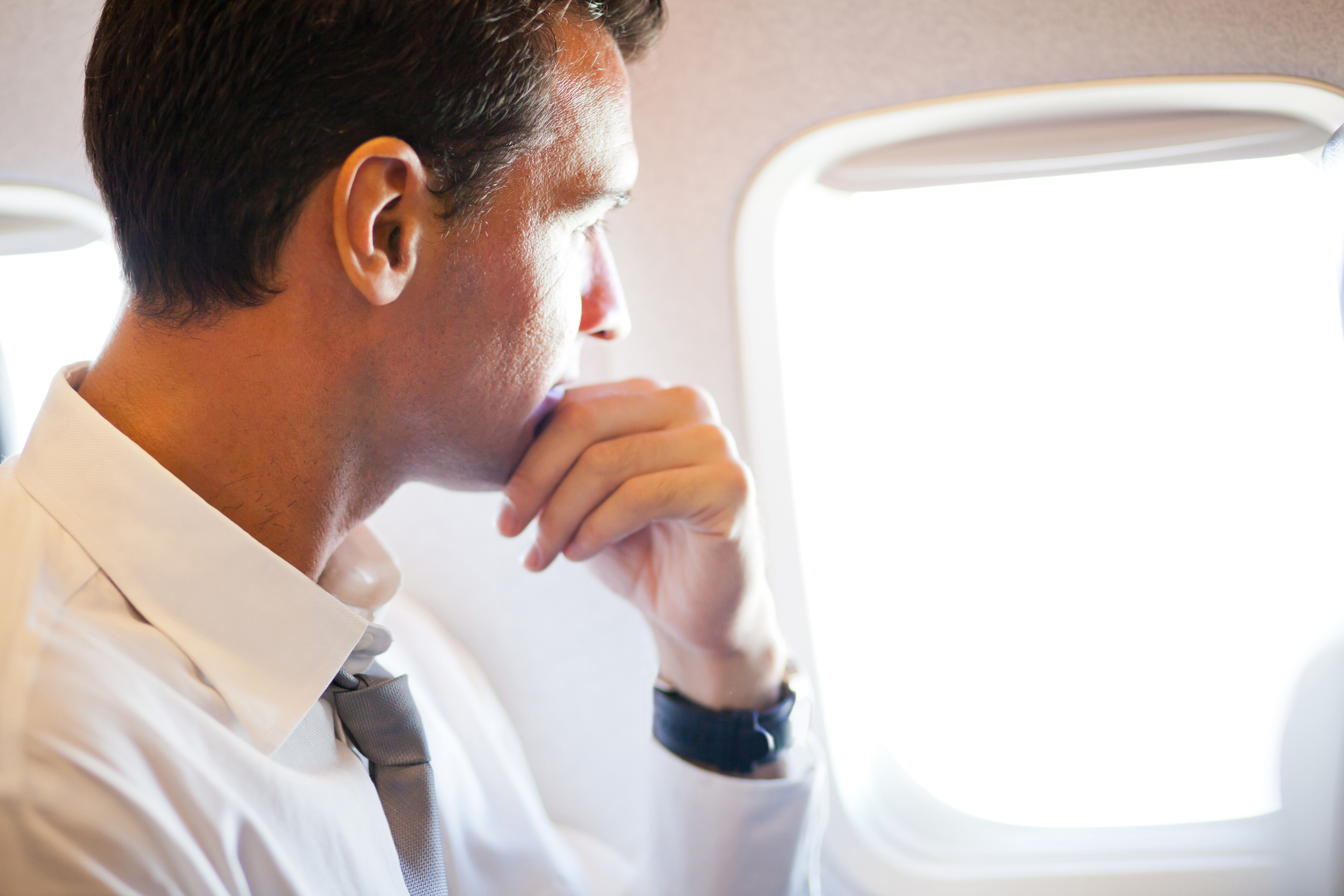 Hombre de negocios serio dentro de un avión mirando por la ventanilla | Fuente: Shutterstock