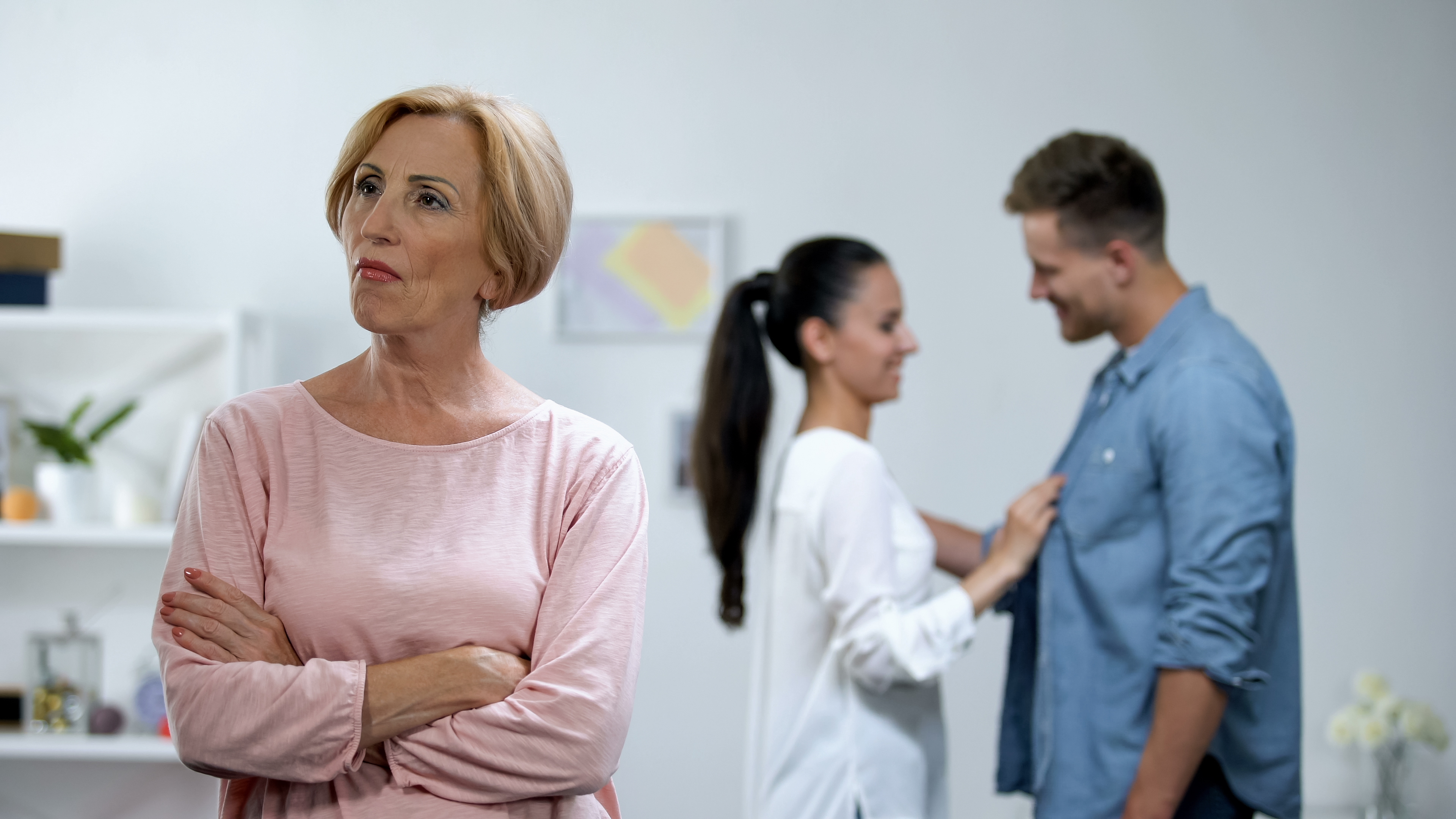 Una suegra de brazos cruzados con su hijo y su nuera que aparecen felices al fondo | Foto: Shutterstock