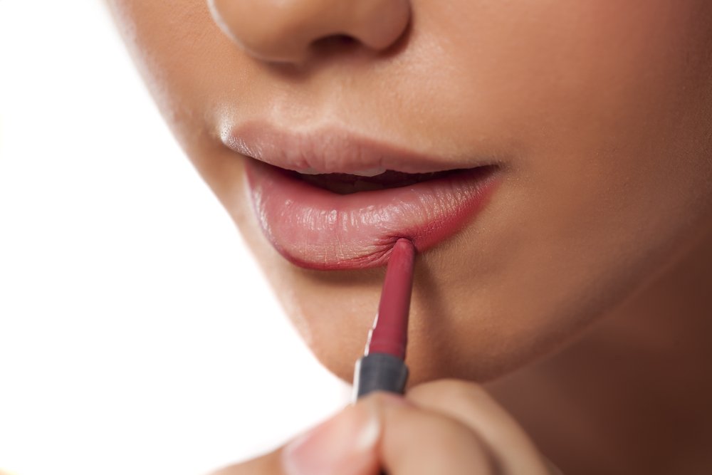 Mujer delineando sus labios con un tono medio. | Foto: Shutterstock