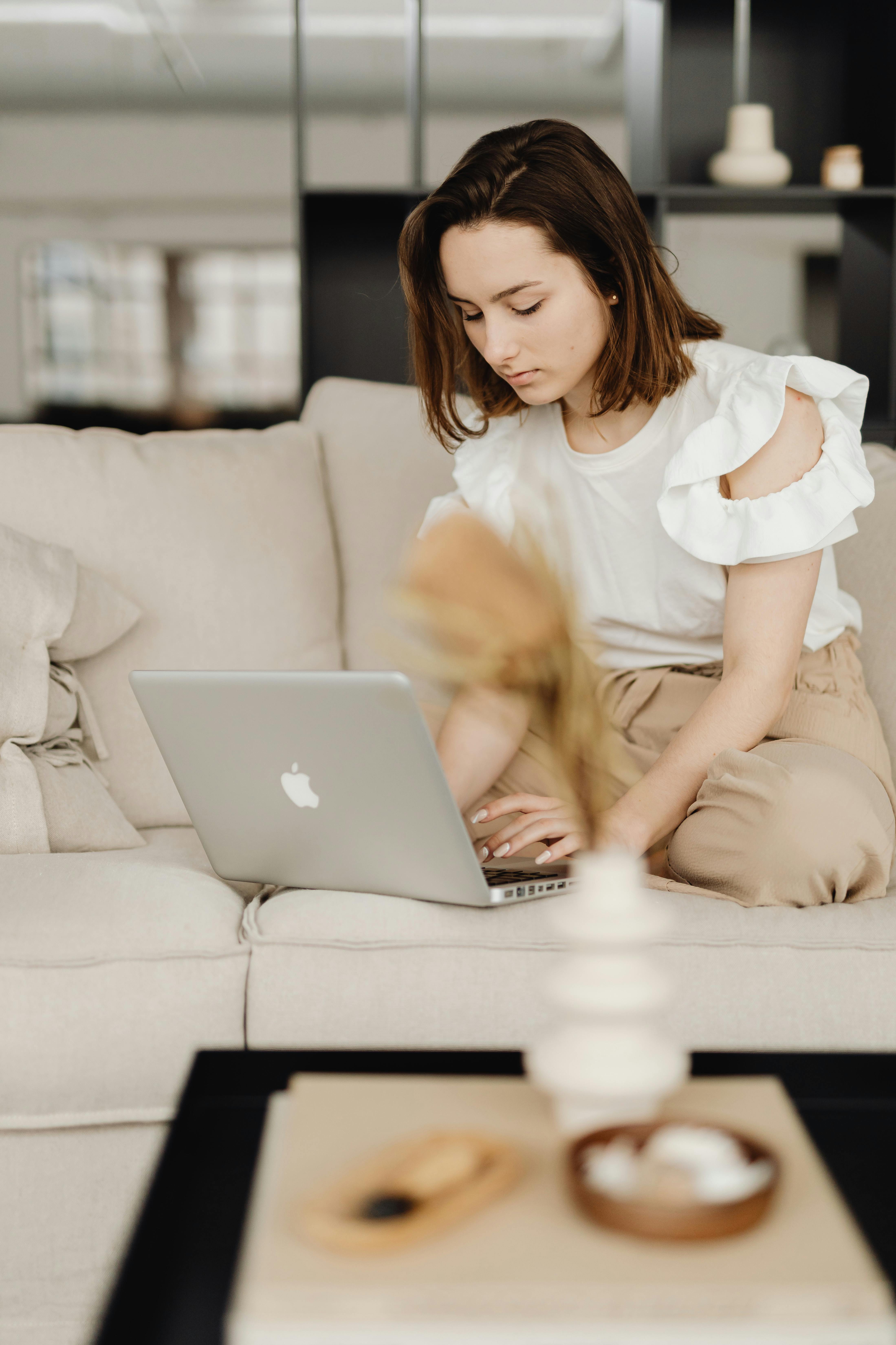 Una mujer en el sofá tecleando en un Macbook | Fuente: Pexels