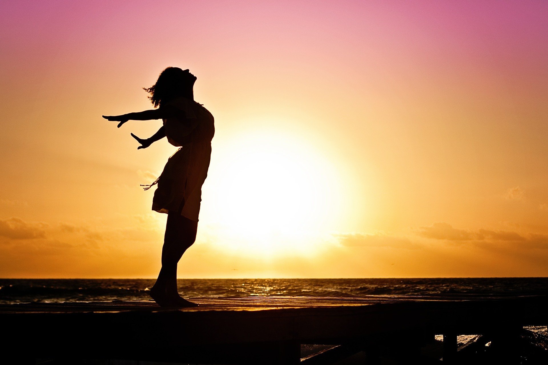 Mujer estirando los brazos a la orilla del mar. | Foto: Pixabay