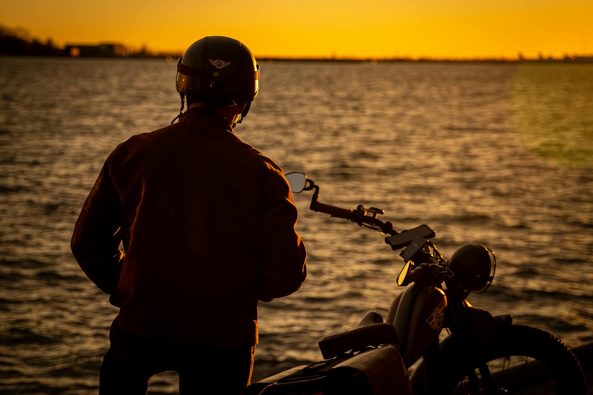 Silueta de un hombre de pie en la orilla cerca de su moto | Fuente: Pexels