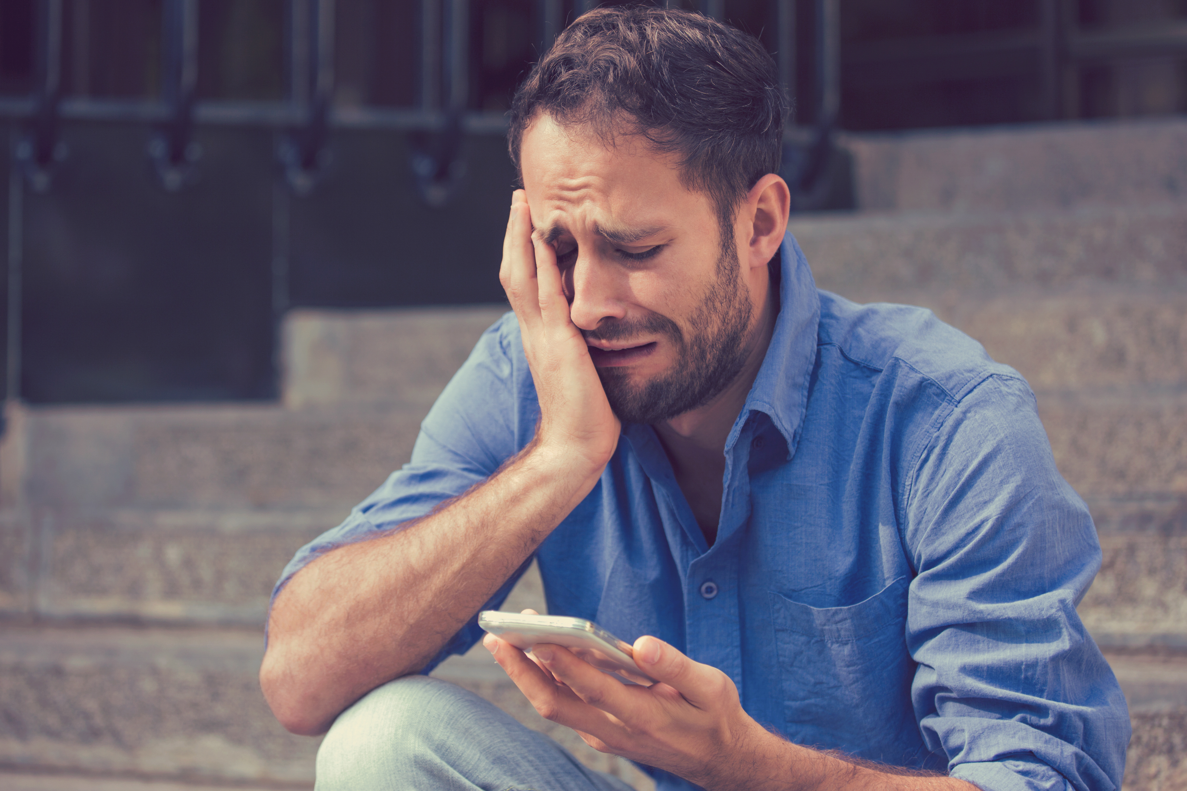 Un hombre solloza mientras mira fijamente su teléfono móvil. | Foto: Shutterstock