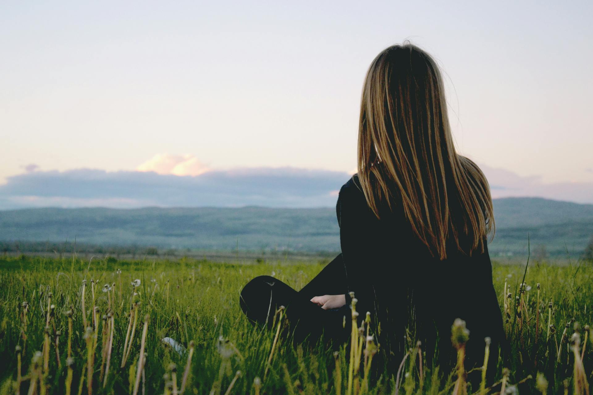 Vista trasera de una mujer sentada en un campo verde | Fuente: Pexels