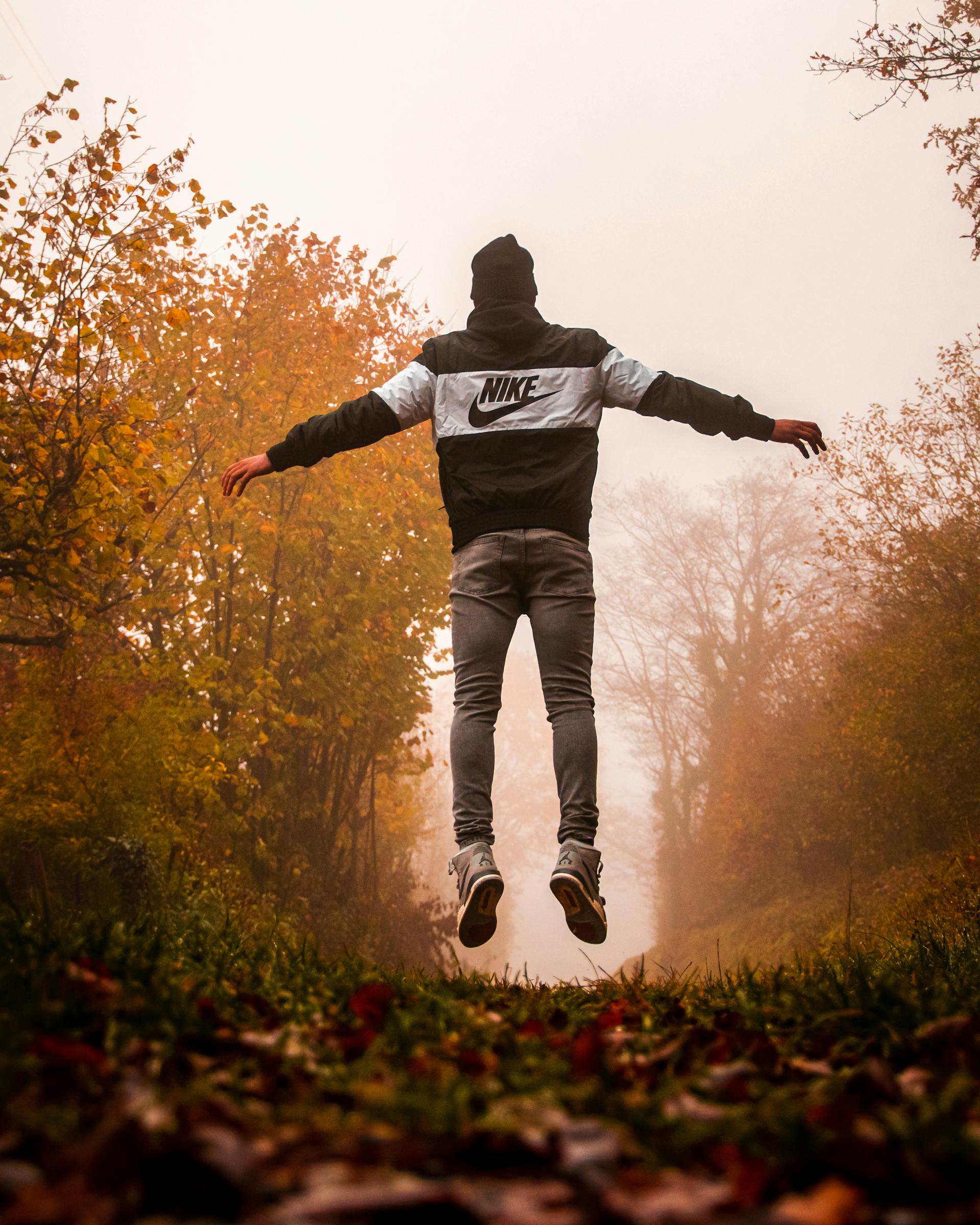 Un hombre con sudadera Nike y pantalones grises saltando en el aire | Fuente: Pexels