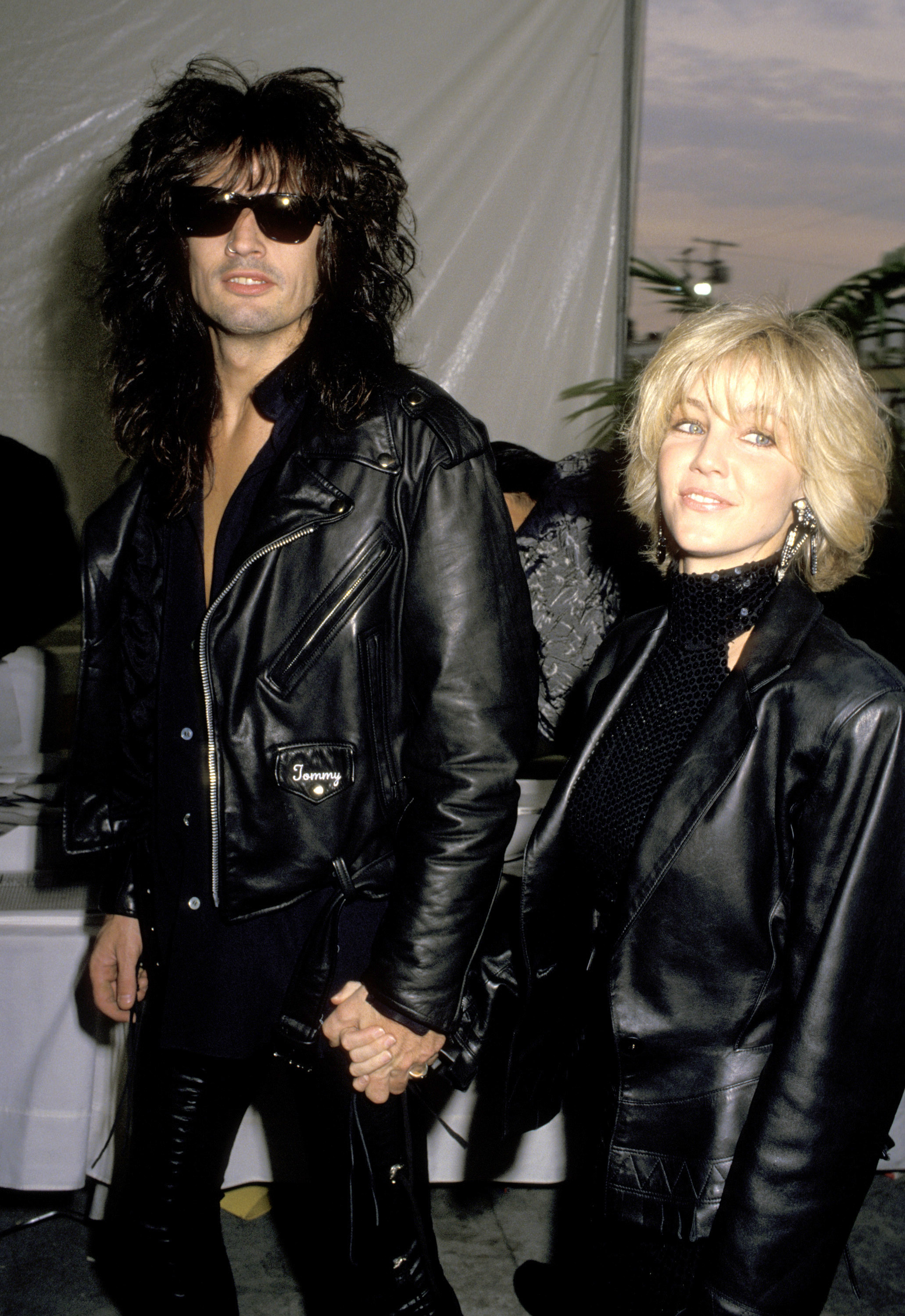 Heather Locklear y su entonces esposo, Tommy Lee, hacen una entrada espectacular tomados de la mano en la 32.ª edición de los Premios Grammy, el 21 de febrero de 1990. Esta pareja estrella del rock and roll va a juego vestida de cuero negro de pies a cabeza: Lee lleva lentes de sol oscuros y una chaqueta motera bordada, mientras que Locklear estrena un corte bob rubio con textura, aretes largos y un top de cuello alto con lentejuelas bajo una chaqueta de cuero extragrande. | Fuente: Getty Images
