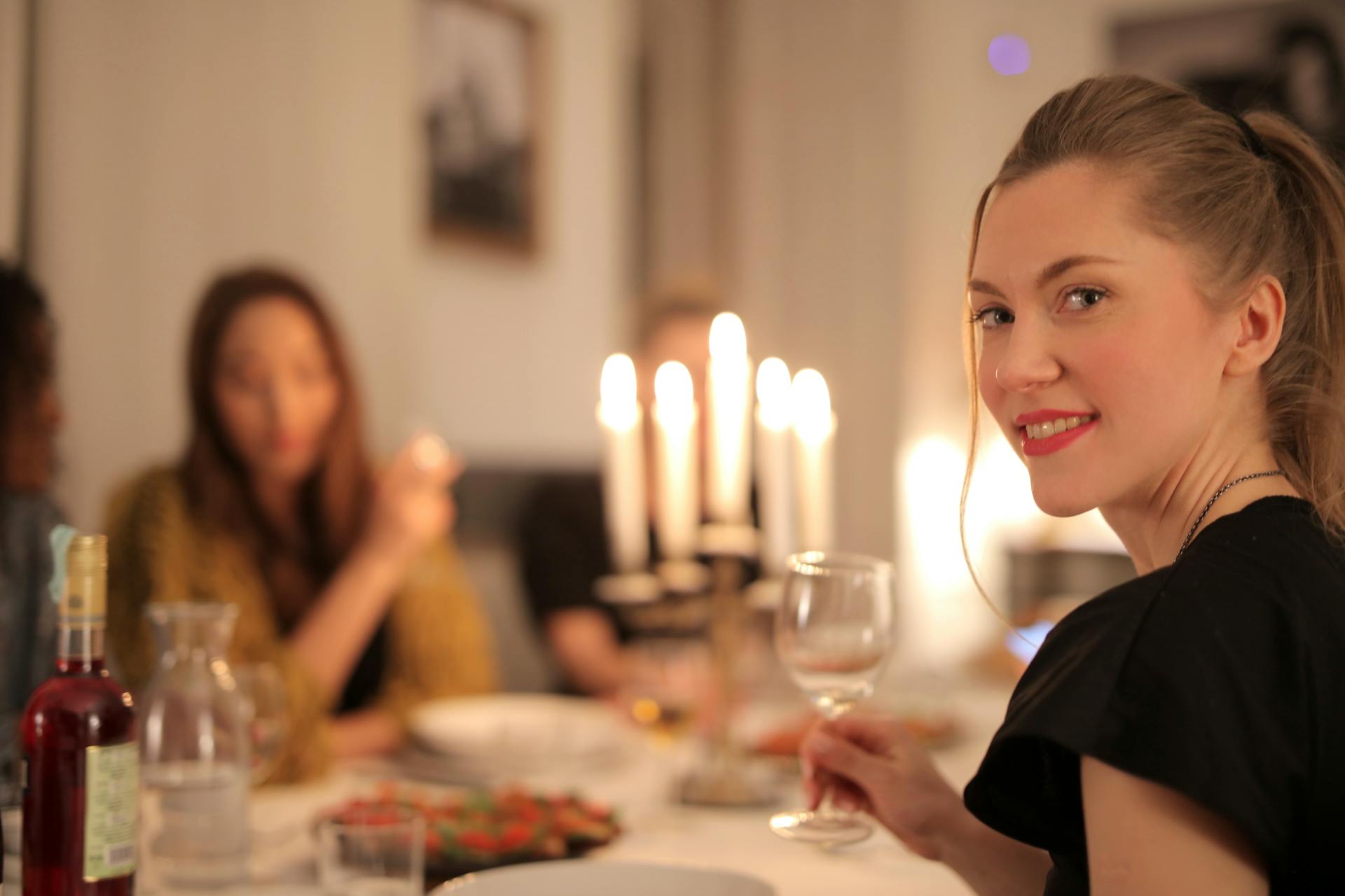 Una mujer sonríe mientras sostiene una copa de vino en la mesa | Fuente: Pexels