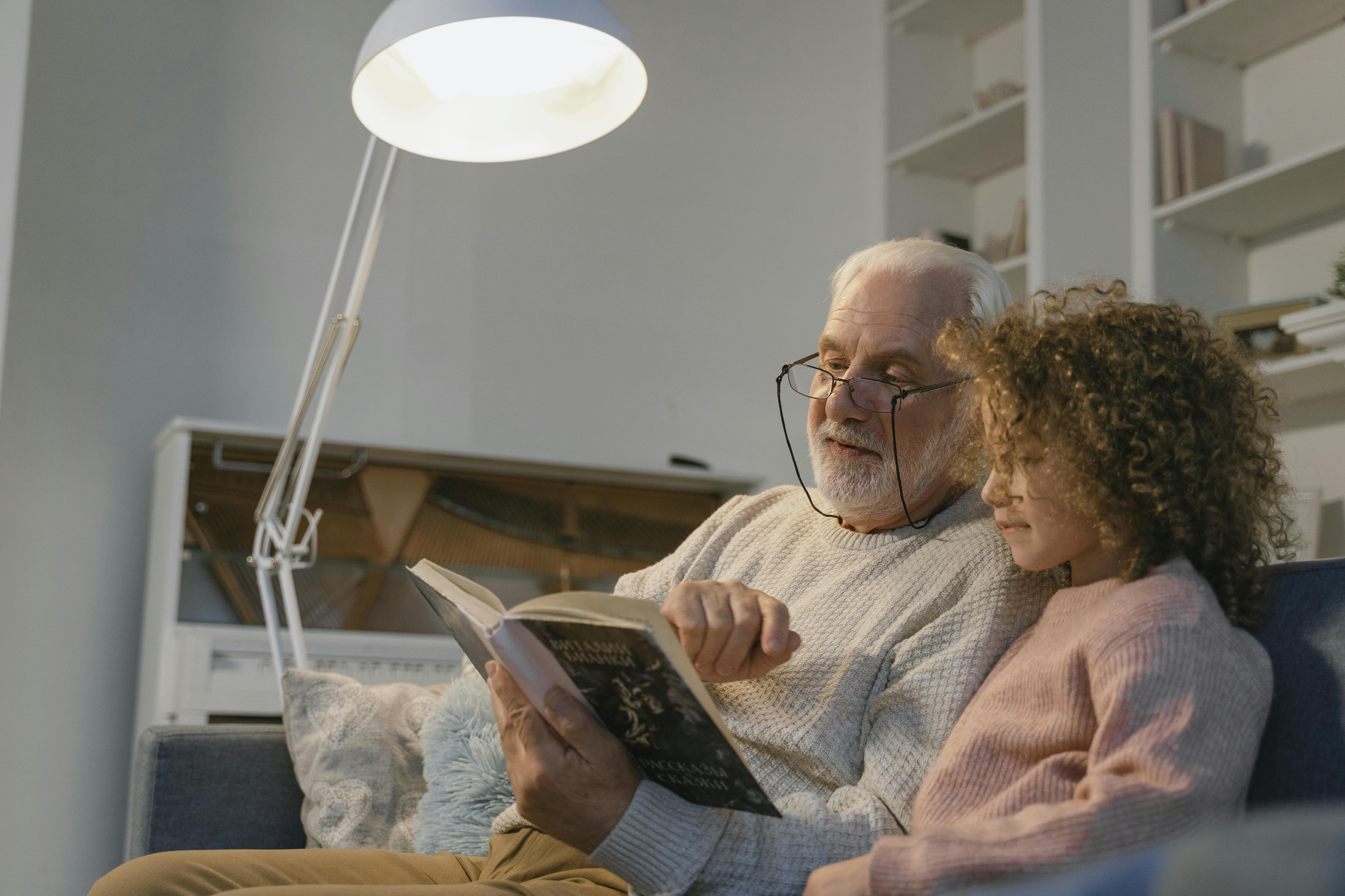 Un abuelo leyendo un libro a su nieta | Foto: Pexels