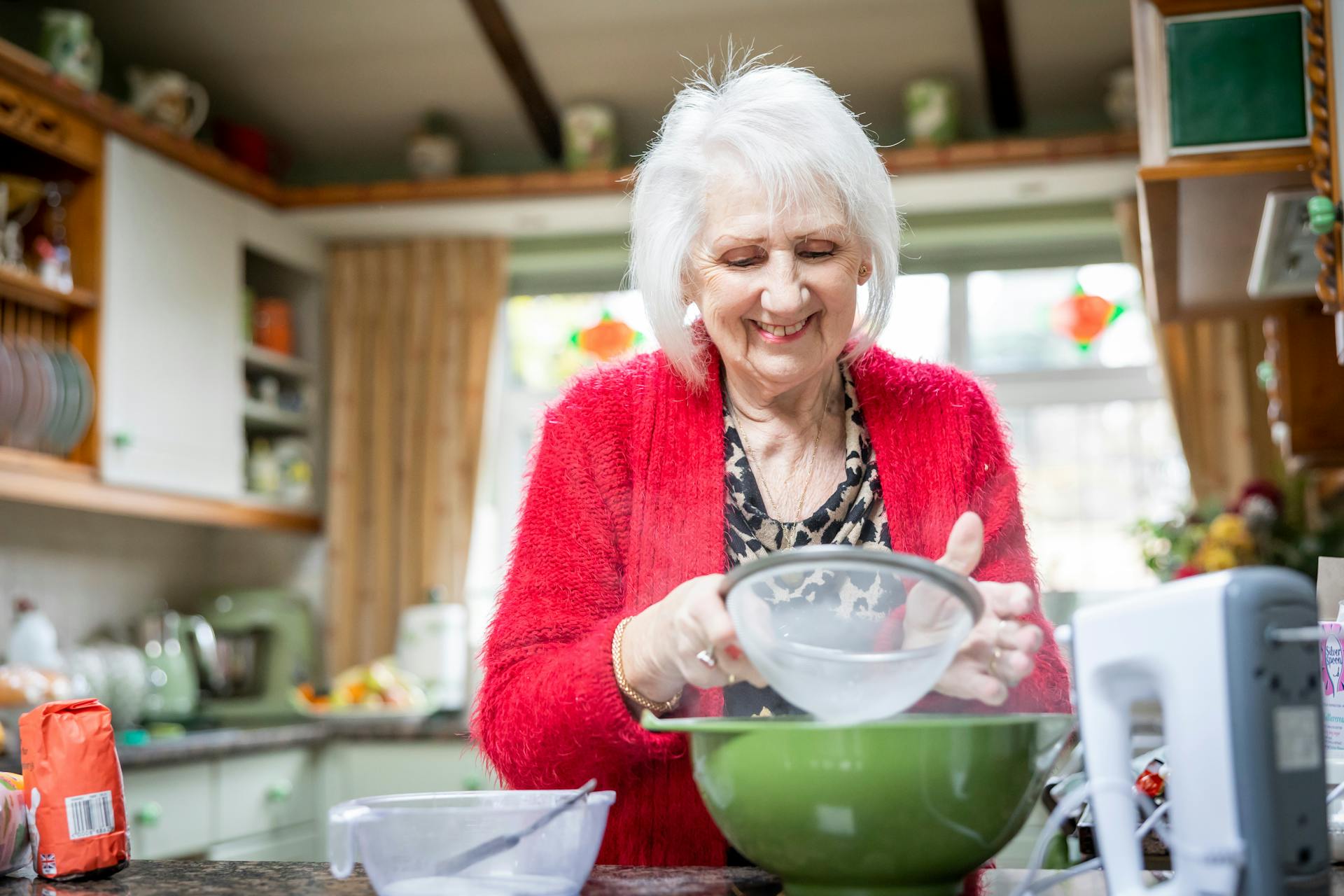 Una anciana sonriente tamizando harina en su cocina | Fuente: Pexels