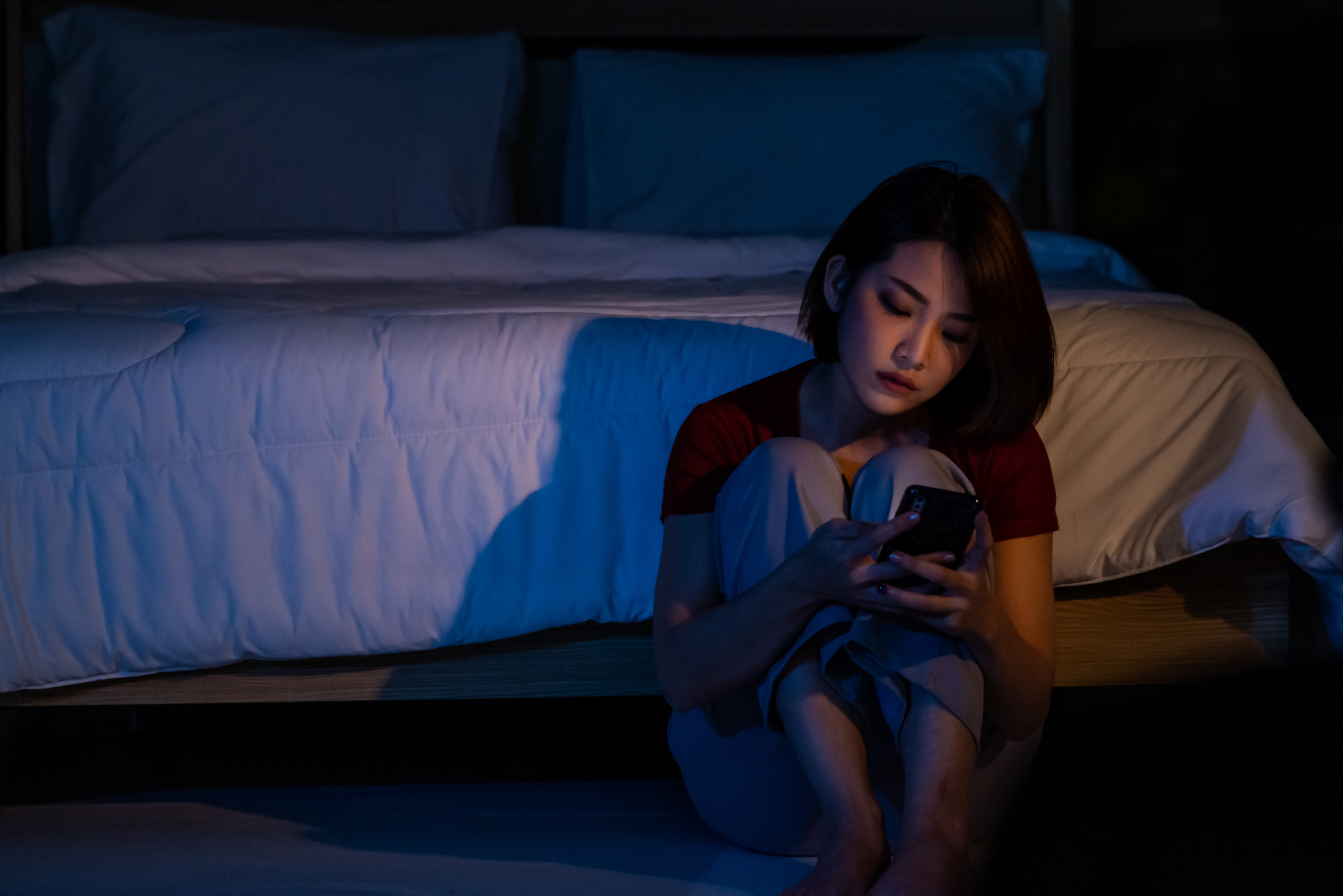 Joven deprimida sentada sola en el suelo del dormitorio mirando el smartphone | Foto: Getty Images