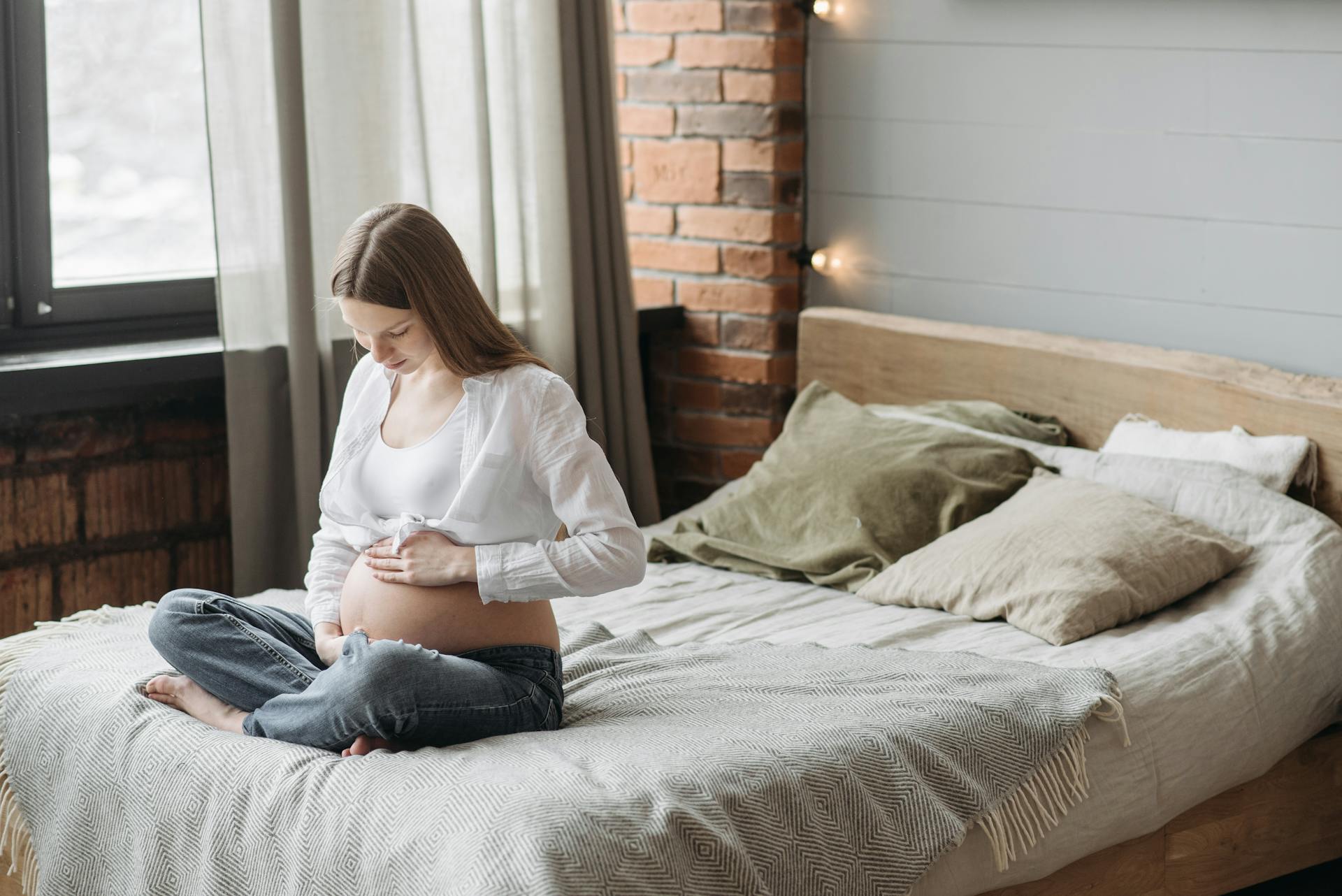 Una mujer embarazada sentada en la cama sujetándose el vientre | Fuente: Pexels