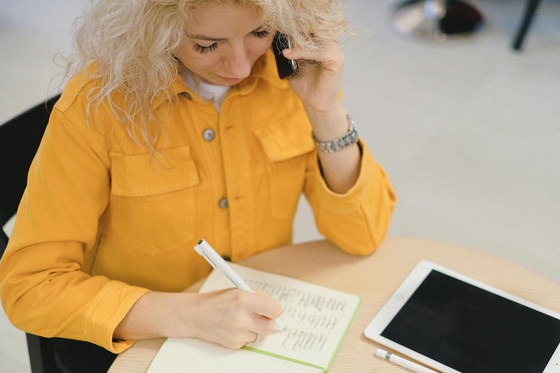 Una mujer escribiendo en su cuaderno mientras atiende una llamada | Fuente: Pexels