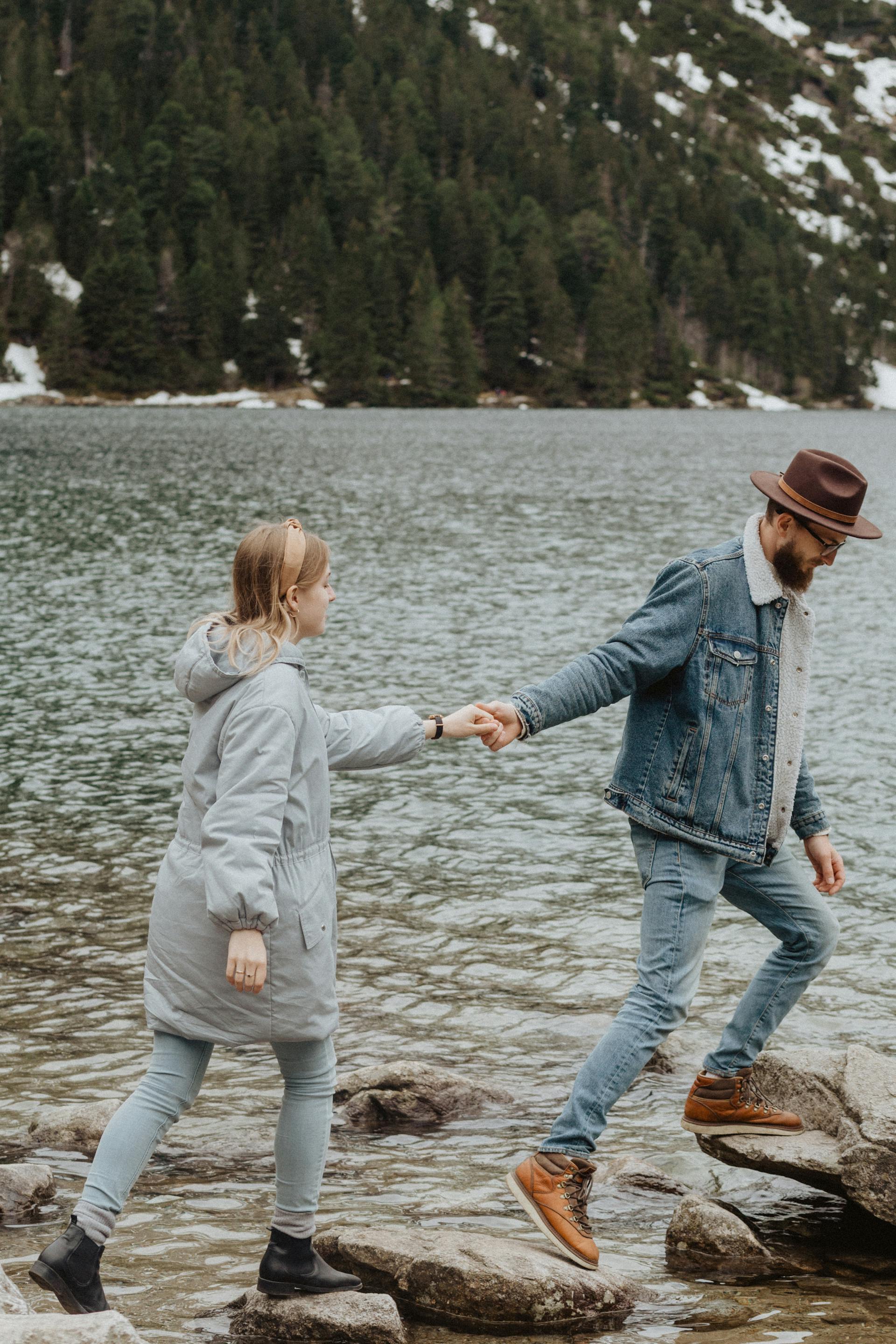 Una pareja paseando sobre las rocas cerca de un lago | Fuente: Pexels