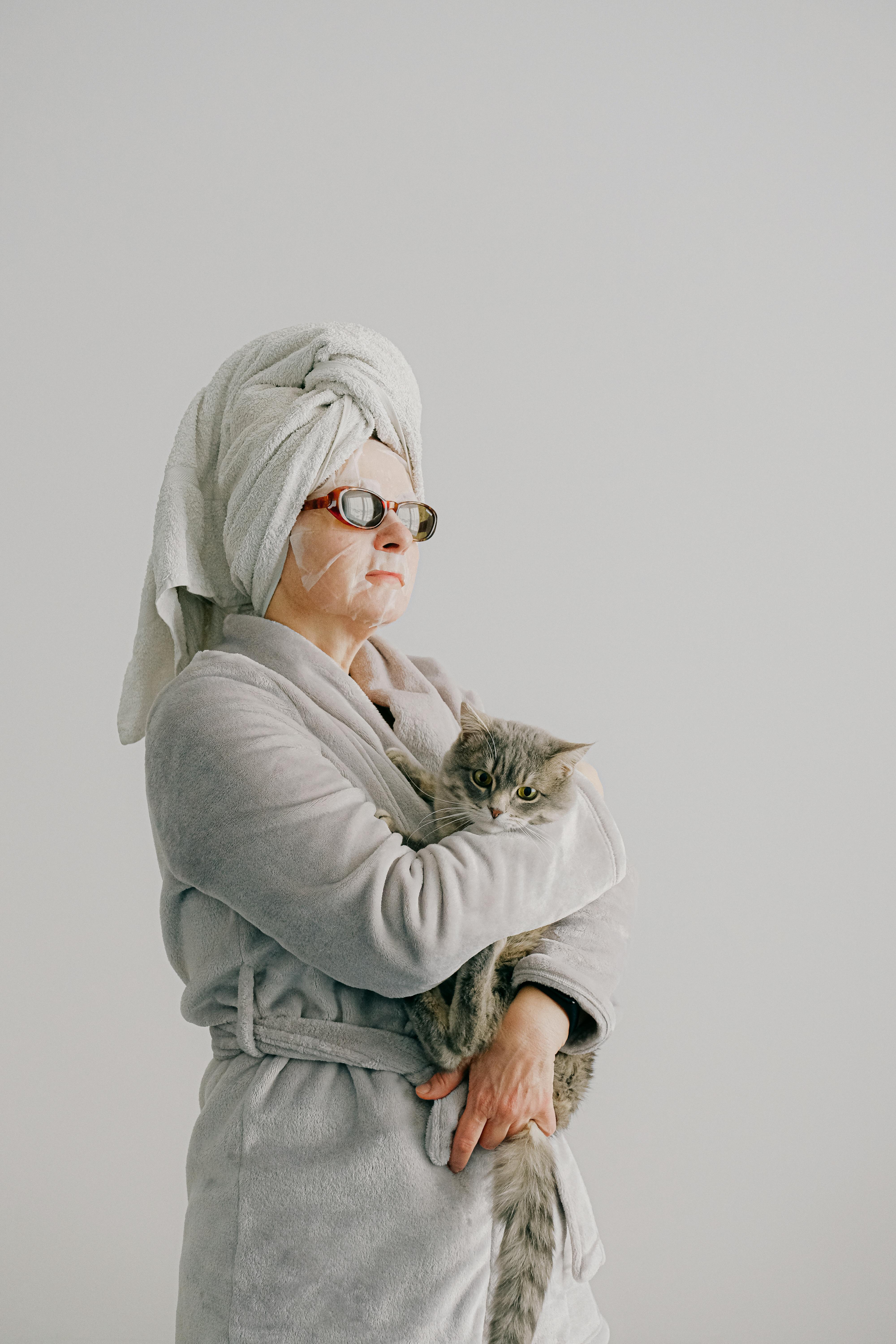 Una mujer arrogante vestida con bata y gafas de sol mientras sostiene un gato | Fuente: Pexels