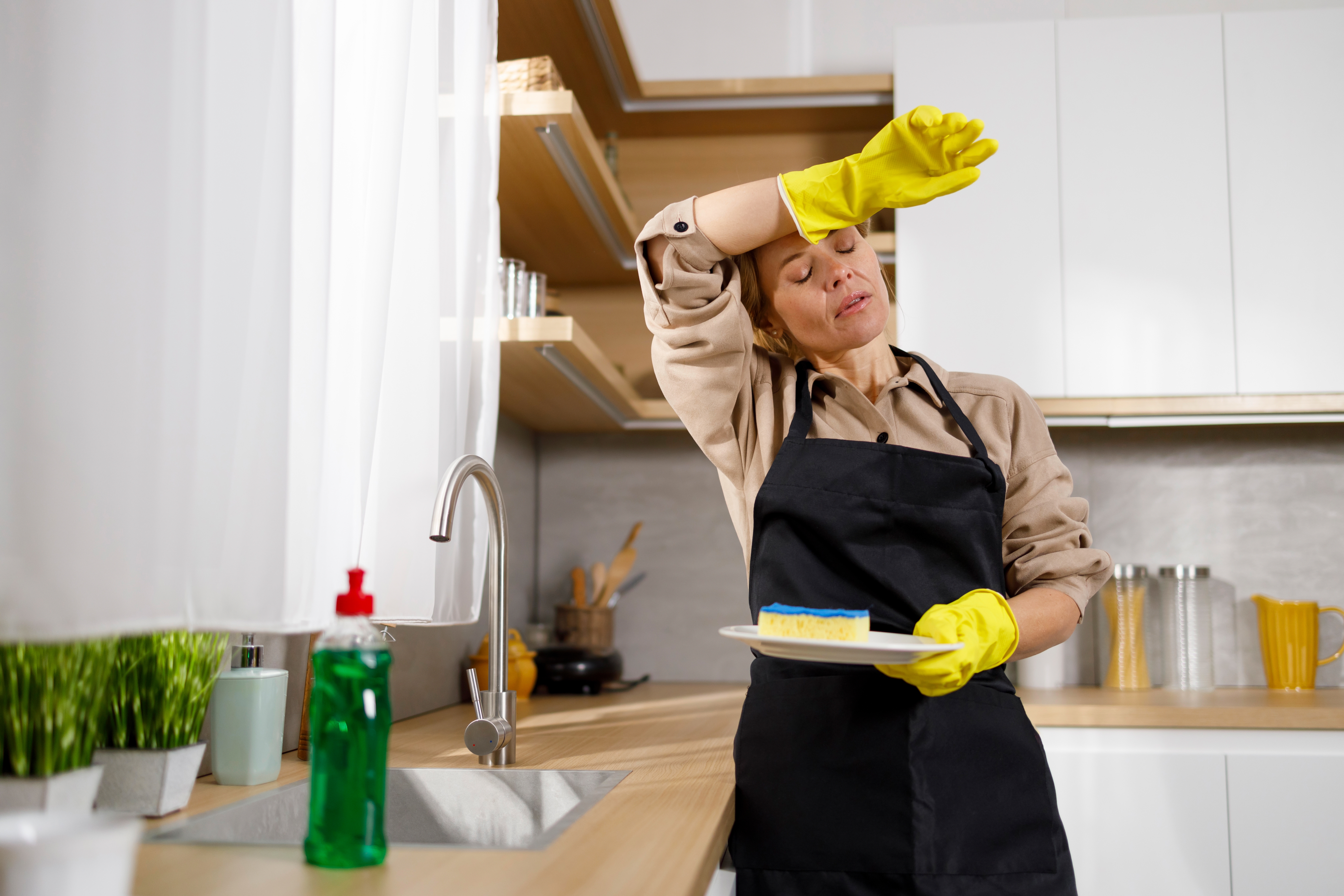 Una mujer cansada lavando los platos en la cocina | Foto: Shutterstock