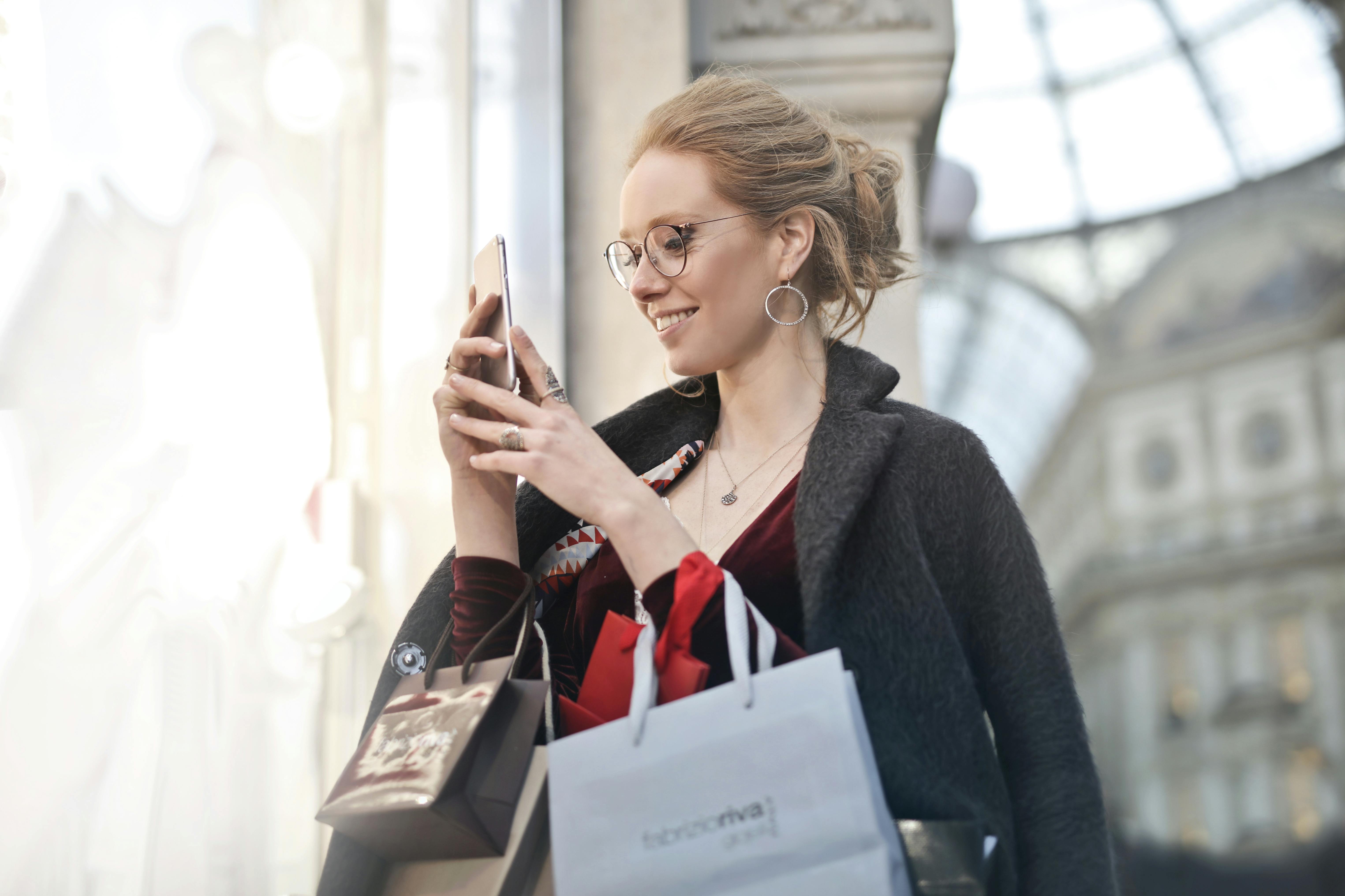 Mujer de compras con su teléfono sonríe | Foto: Pexels