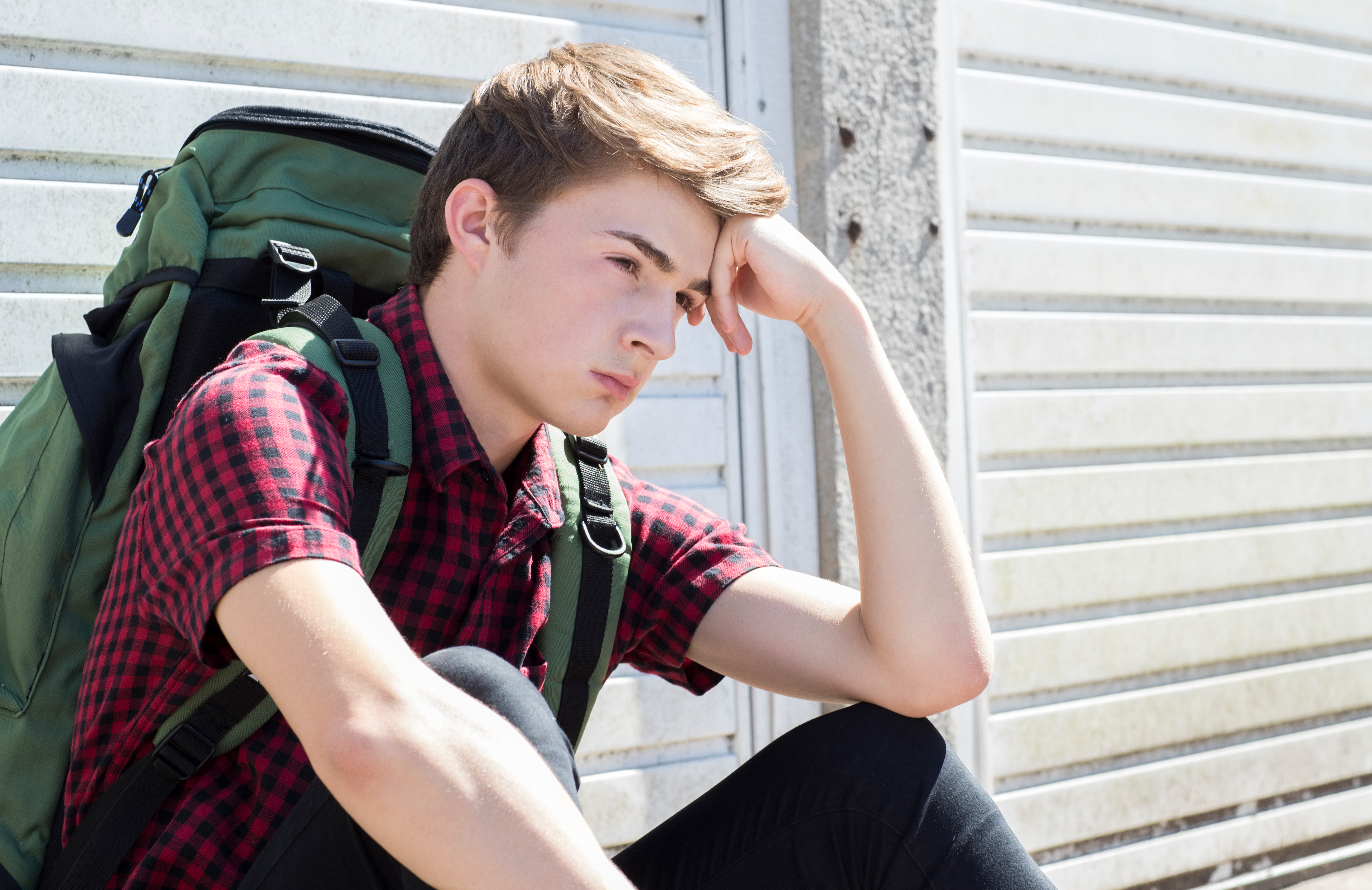 Un adolescente con cara de estresado con mochila sentado en la calle. | Foto: Shutterstock