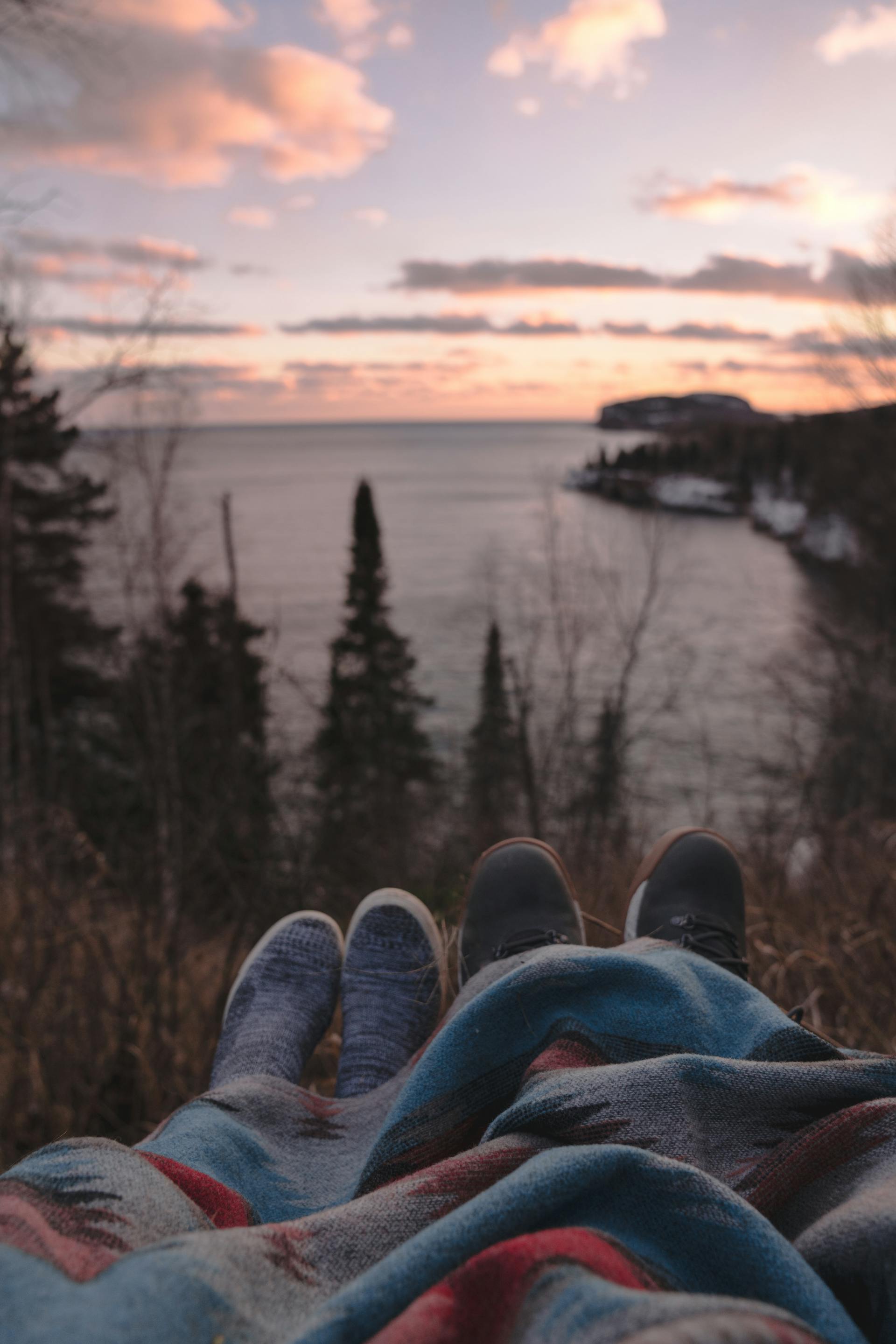 Una pareja anónima tumbada en una colina a la orilla del mar y disfrutando de la puesta de sol | Fuente: Pexels