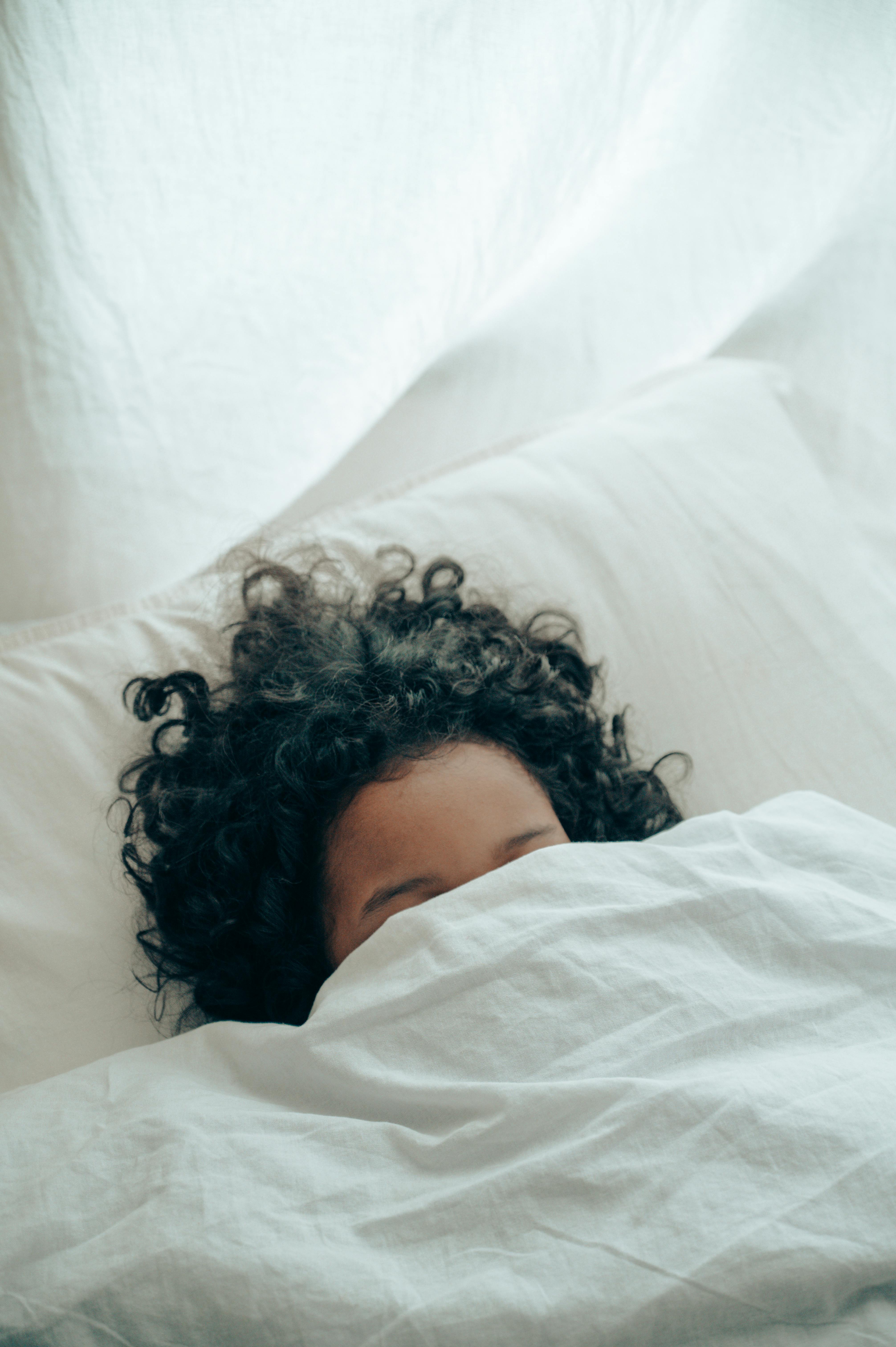 Un niño en la cama agachándose bajo el edredón | Fuente: Pexels
