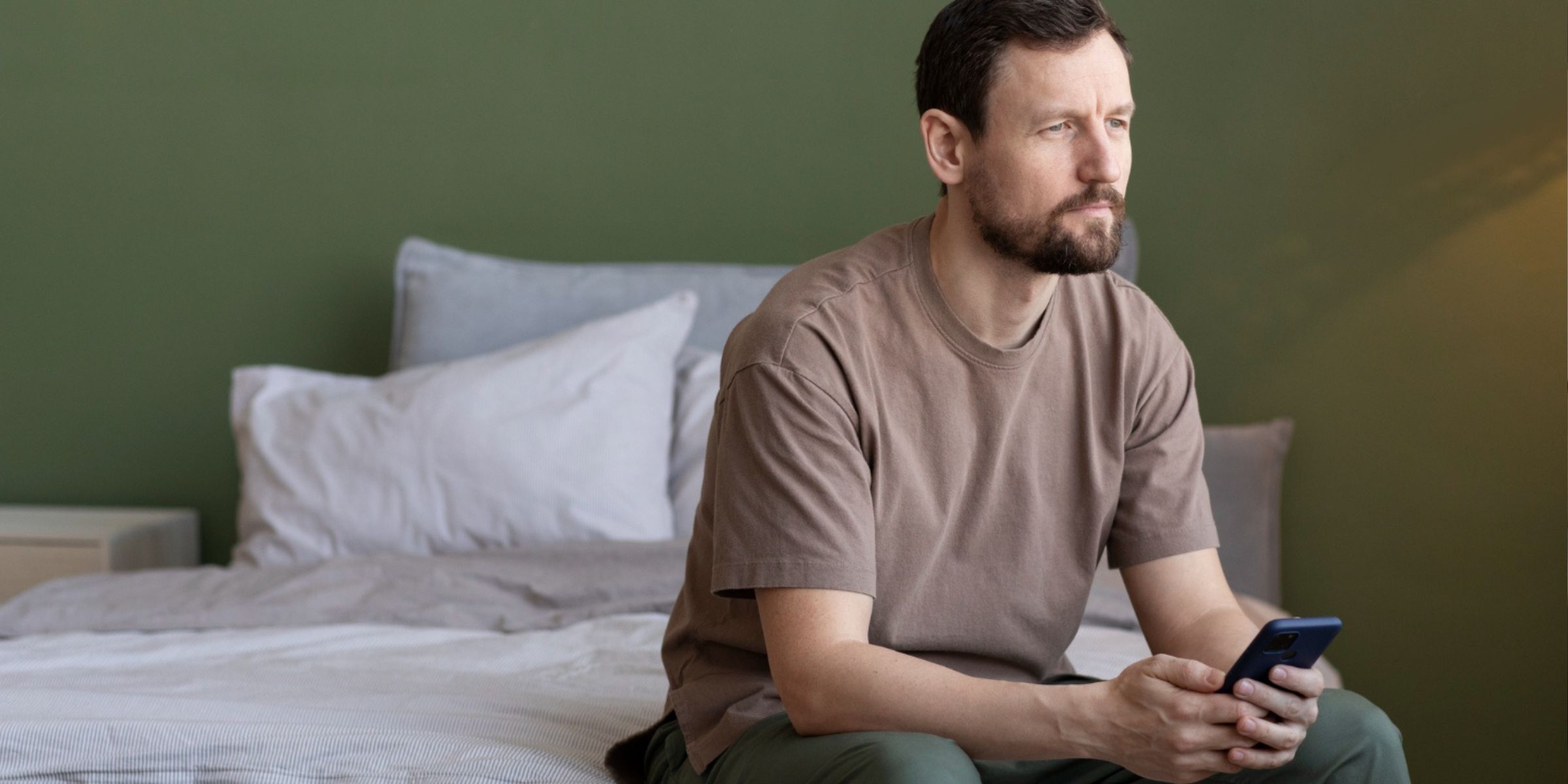 Un hombre con el teléfono en la mano y sentado en la cama | Fuente: Freepik