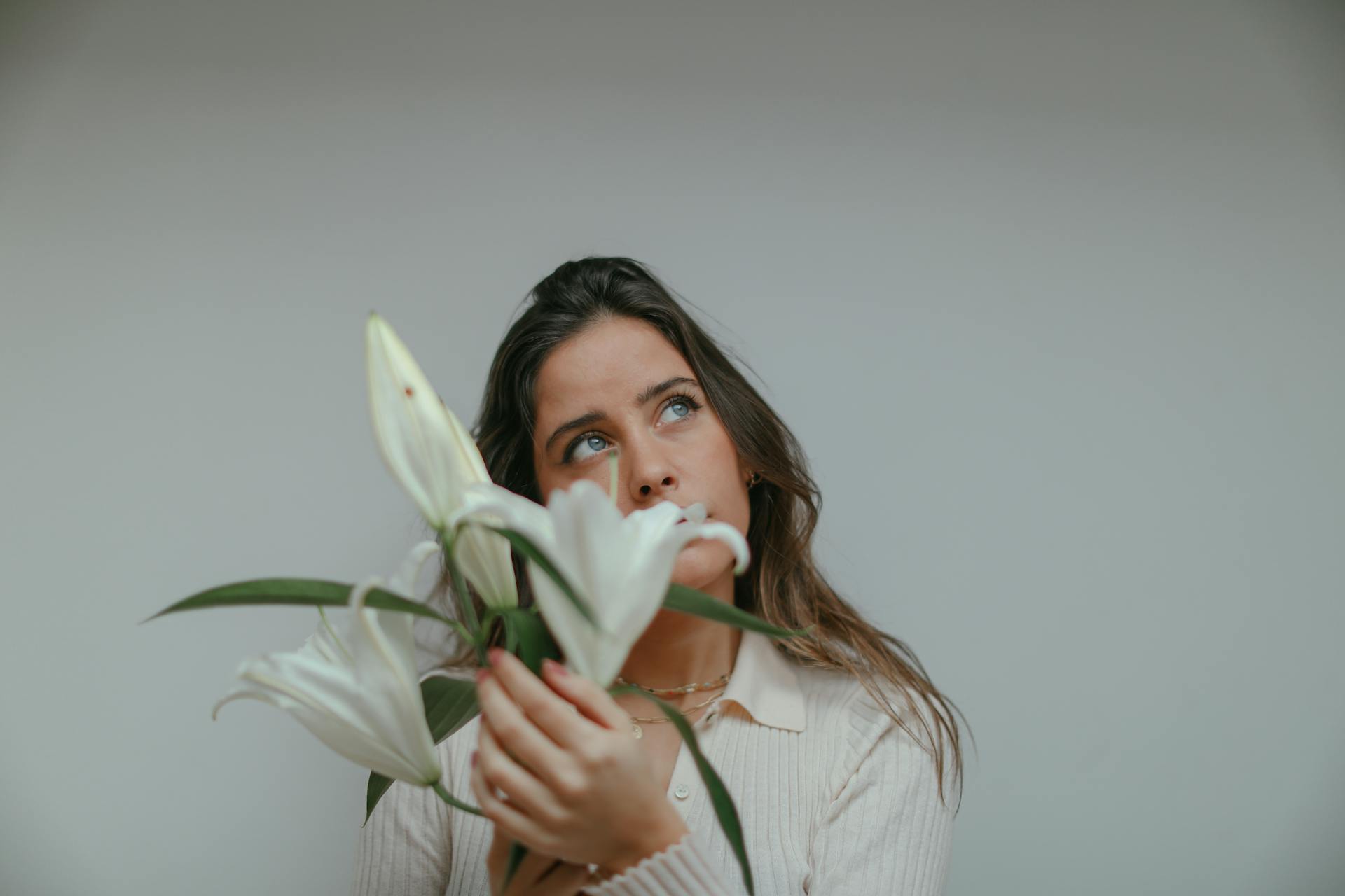 Una donna persa nei suoi pensieri mentre tiene in mano dei gigli bianchi | Fonte: Pexels
