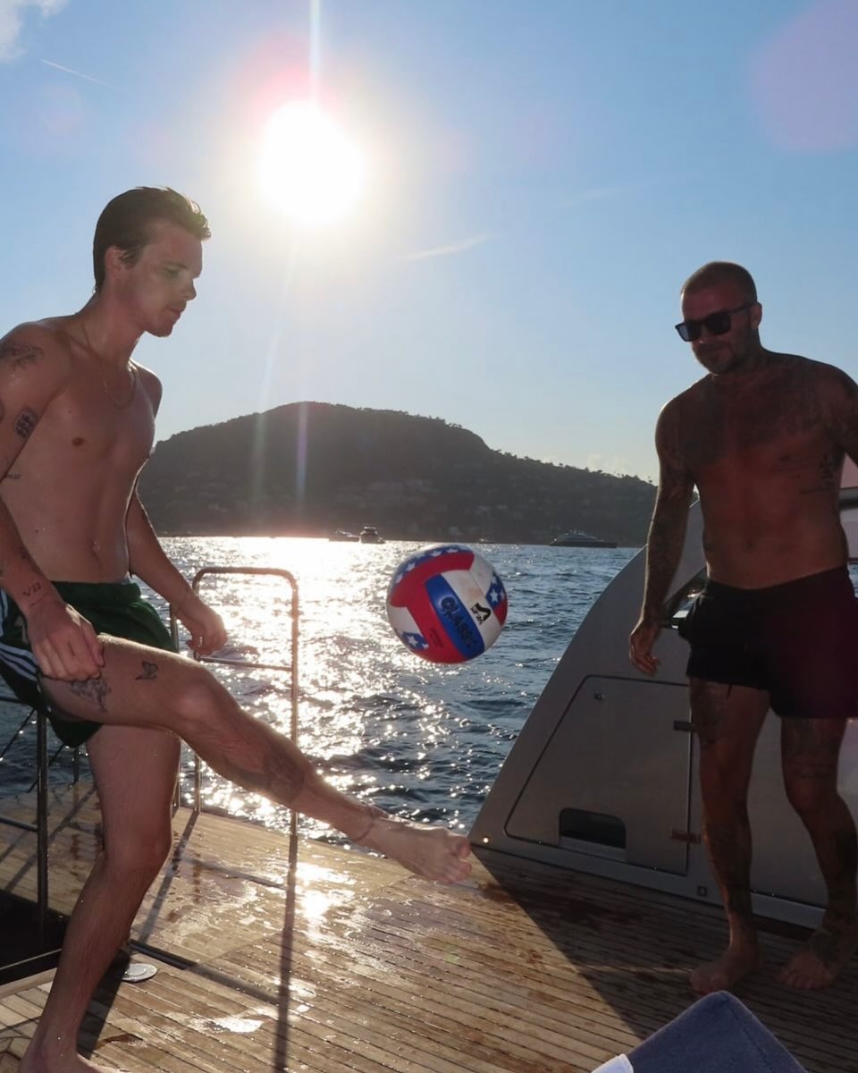 Cruz y David Beckham jugando con un balón de fútbol en un yate, del post de vacaciones de Victoria Beckham del 10 de agosto de 2025 | Fuente: Instagram/victoriabeckham