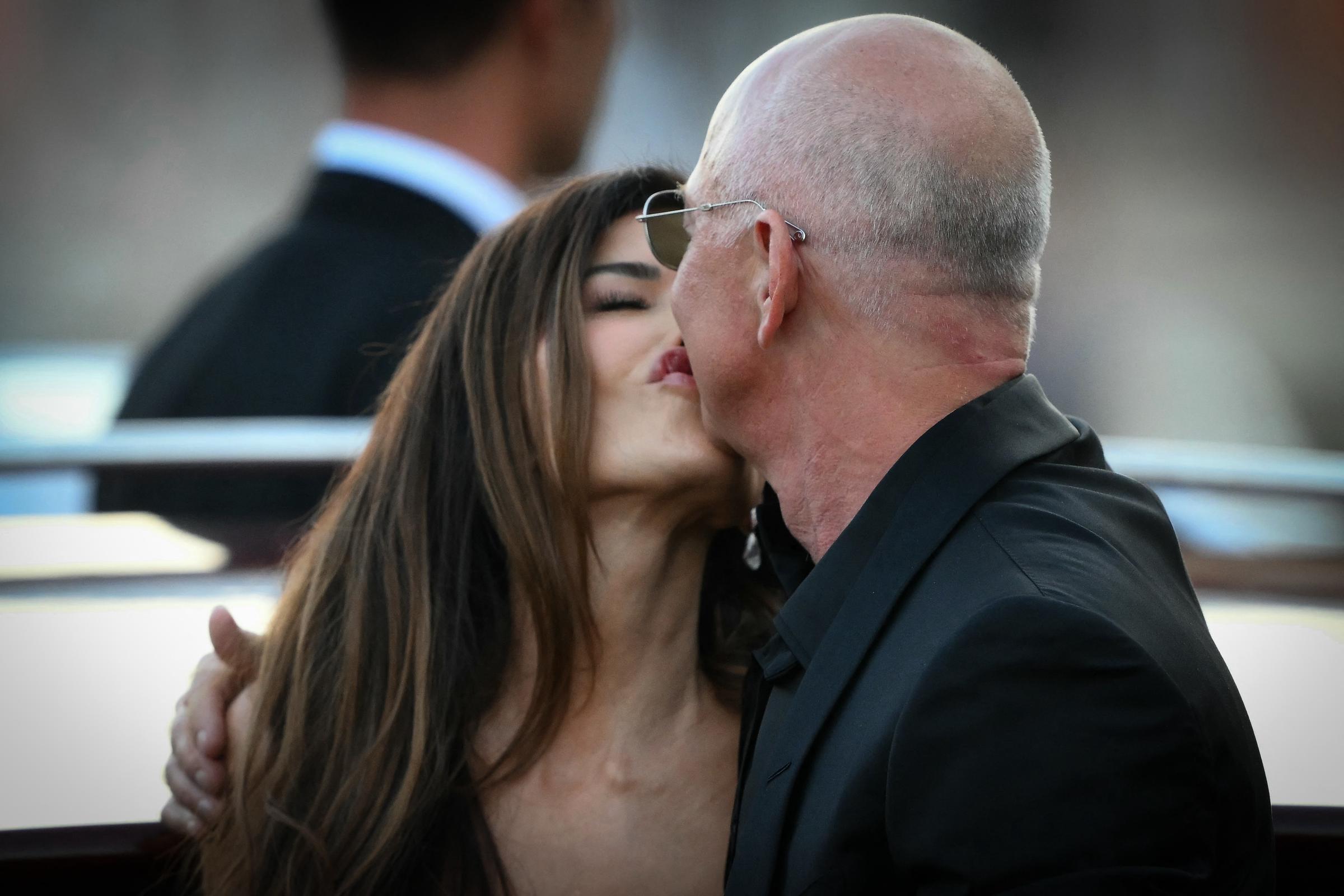 Lauren Sánchez y Jeff Bezos comparten un beso ante la mirada de un guardia trajeado. El cándido momento se desarrolla entre edificios borrosos y la luz del atardecer reflejándose en el agua.