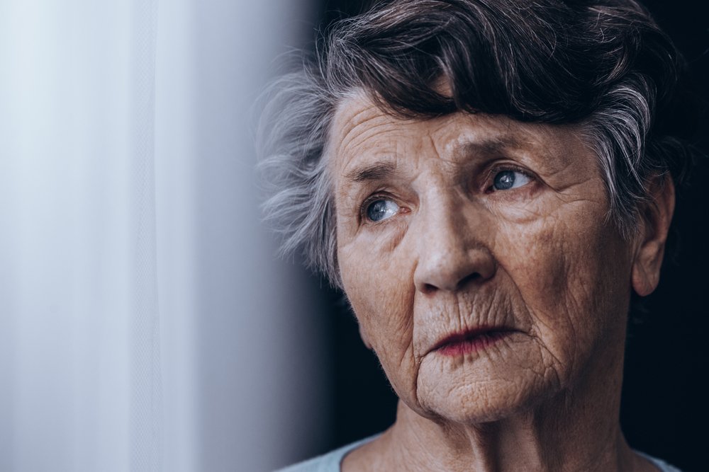 Mujer anciana de pie junto a la ventana. | Fuente: Shutterstock
