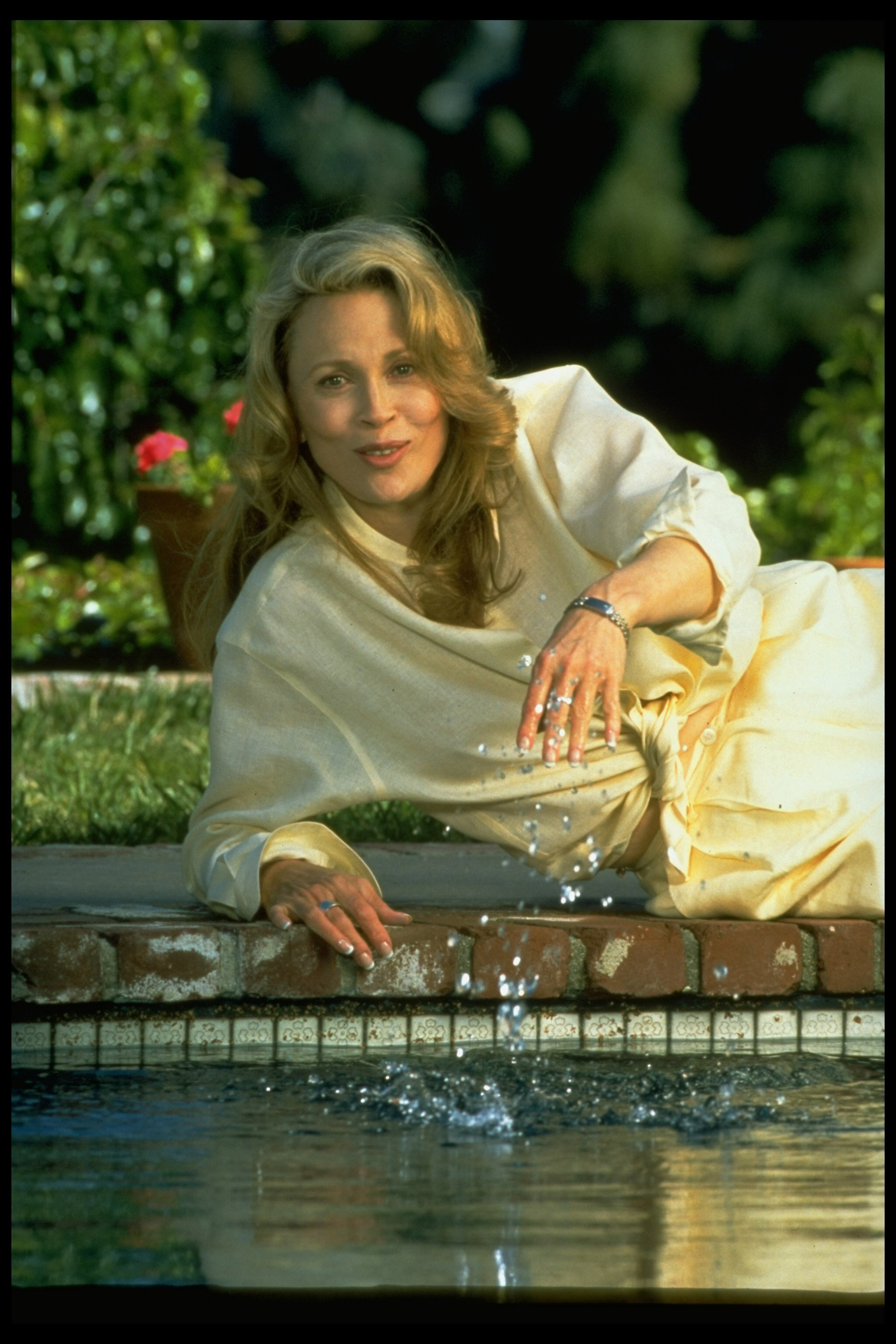 Faye Dunaway tumbada de lado al borde de la piscina de su casa de Hollywood en 1995 | Fuente: Getty Images