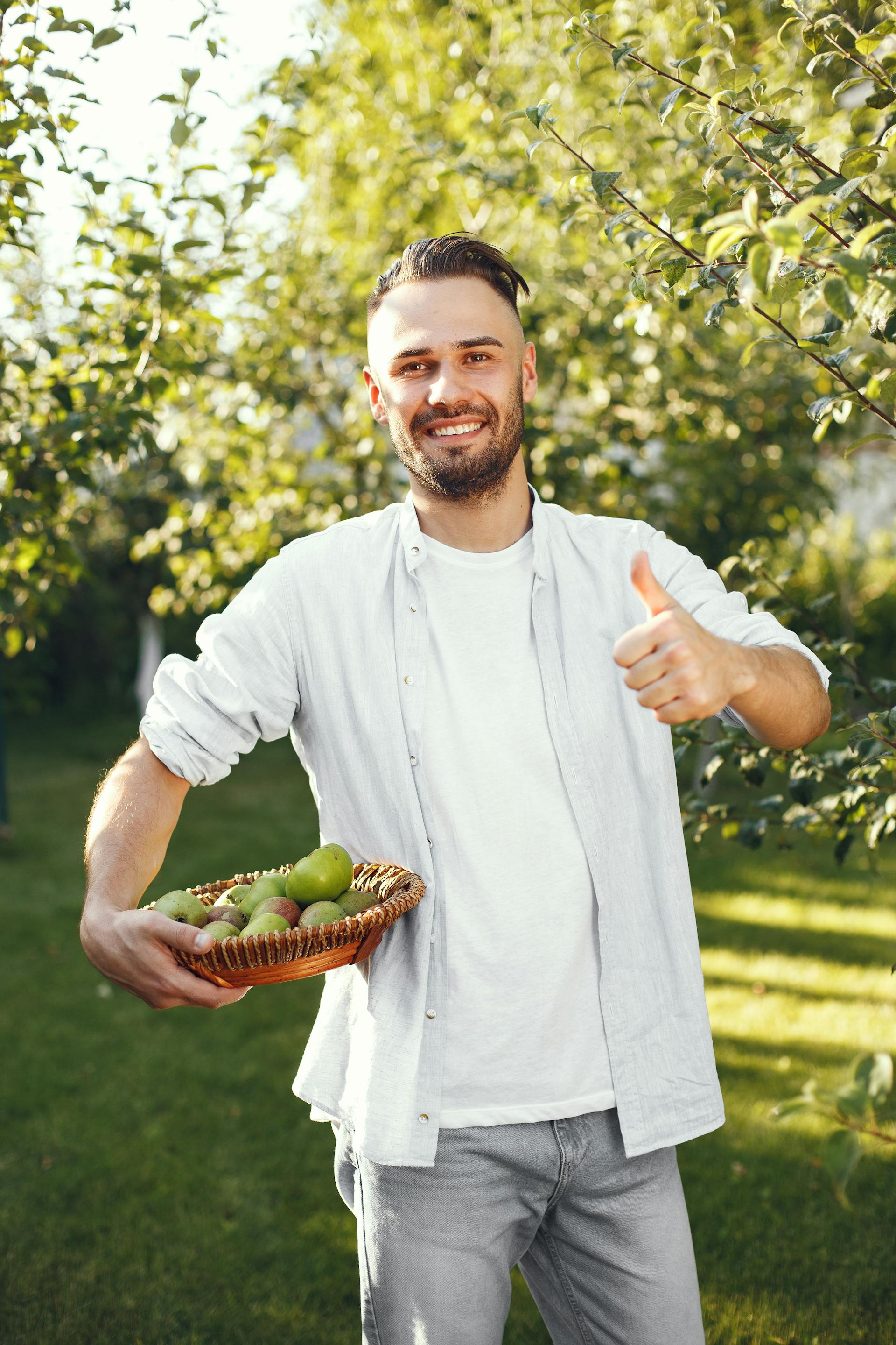 Un hombre de pie en su jardín sujetando una cesta de frutas | Fuente: Pexels