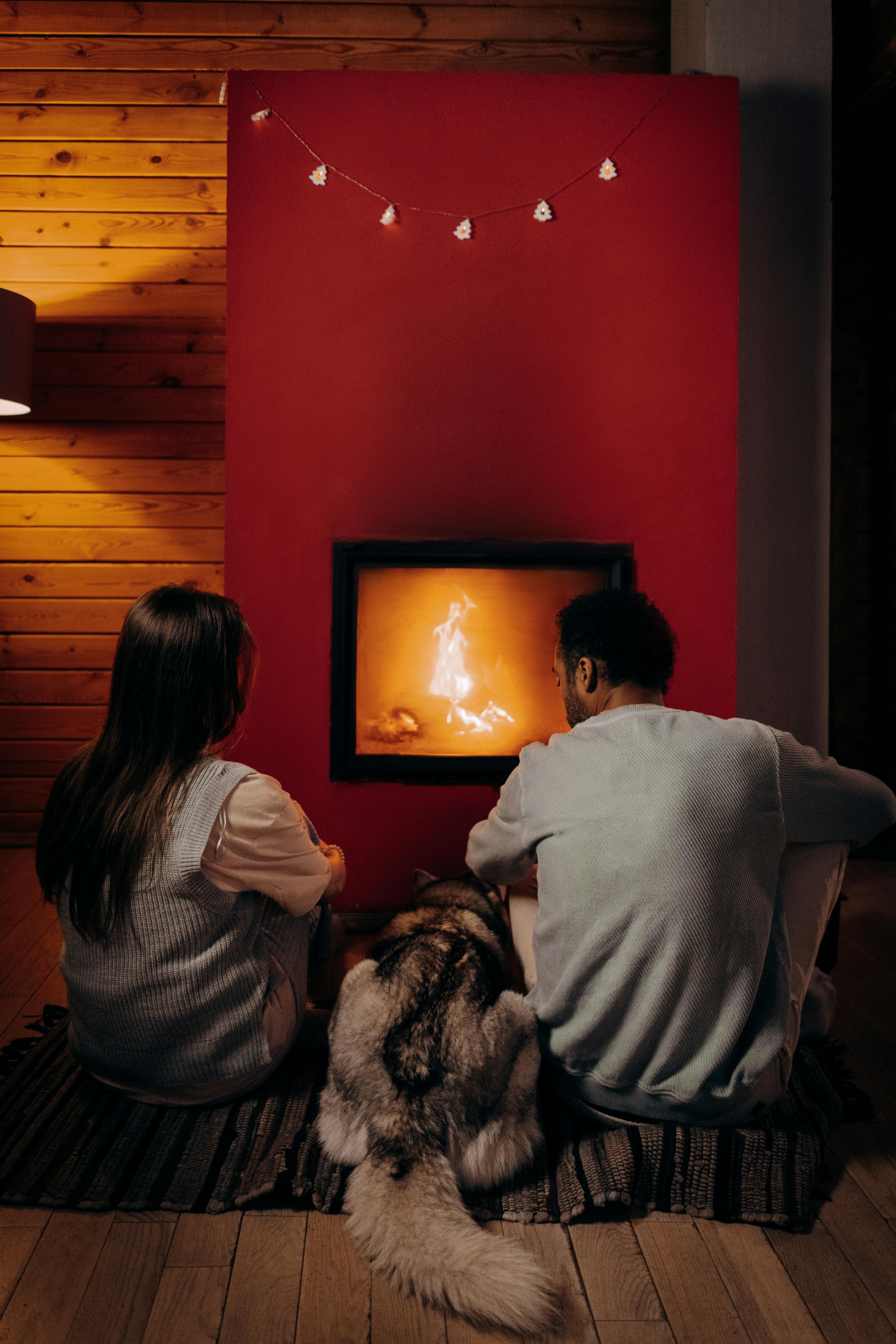 Una pareja sentada cerca de la chimenea con un perro | Fuente: Pexels