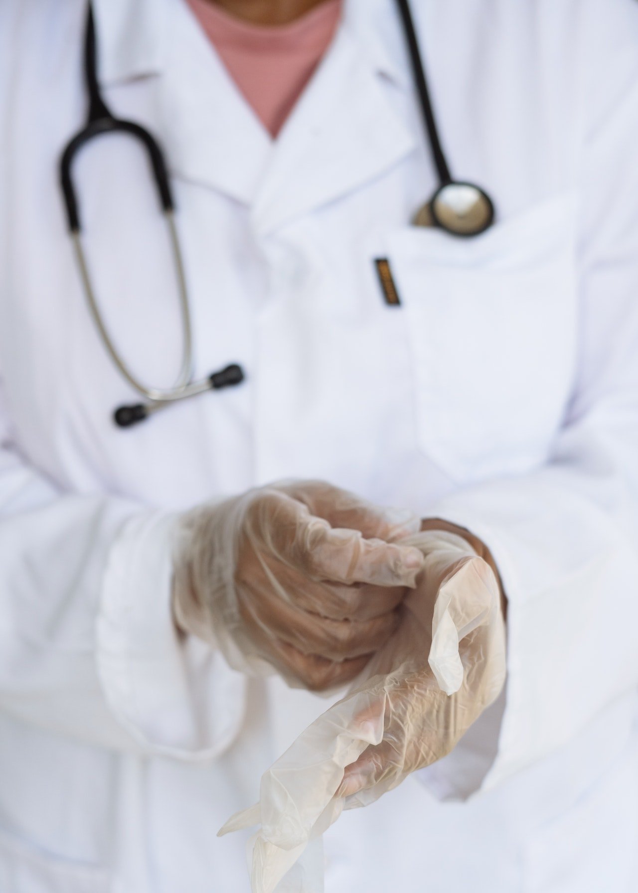 Un médico con bata blanca se quita los guantes. | Foto: Pexels