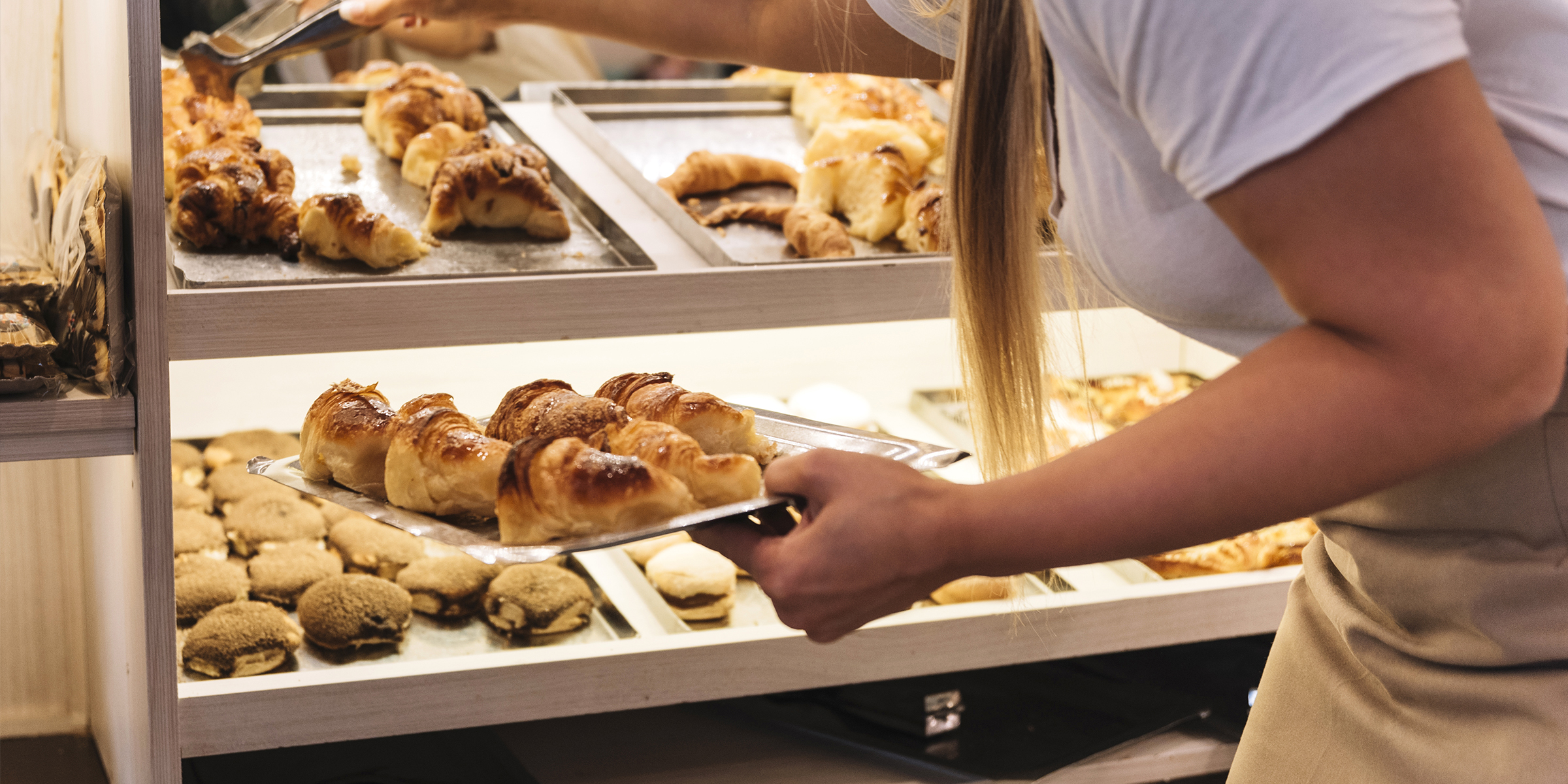 Una mujer surtiendo la vitrina de una panadería | Fuente: Freepik