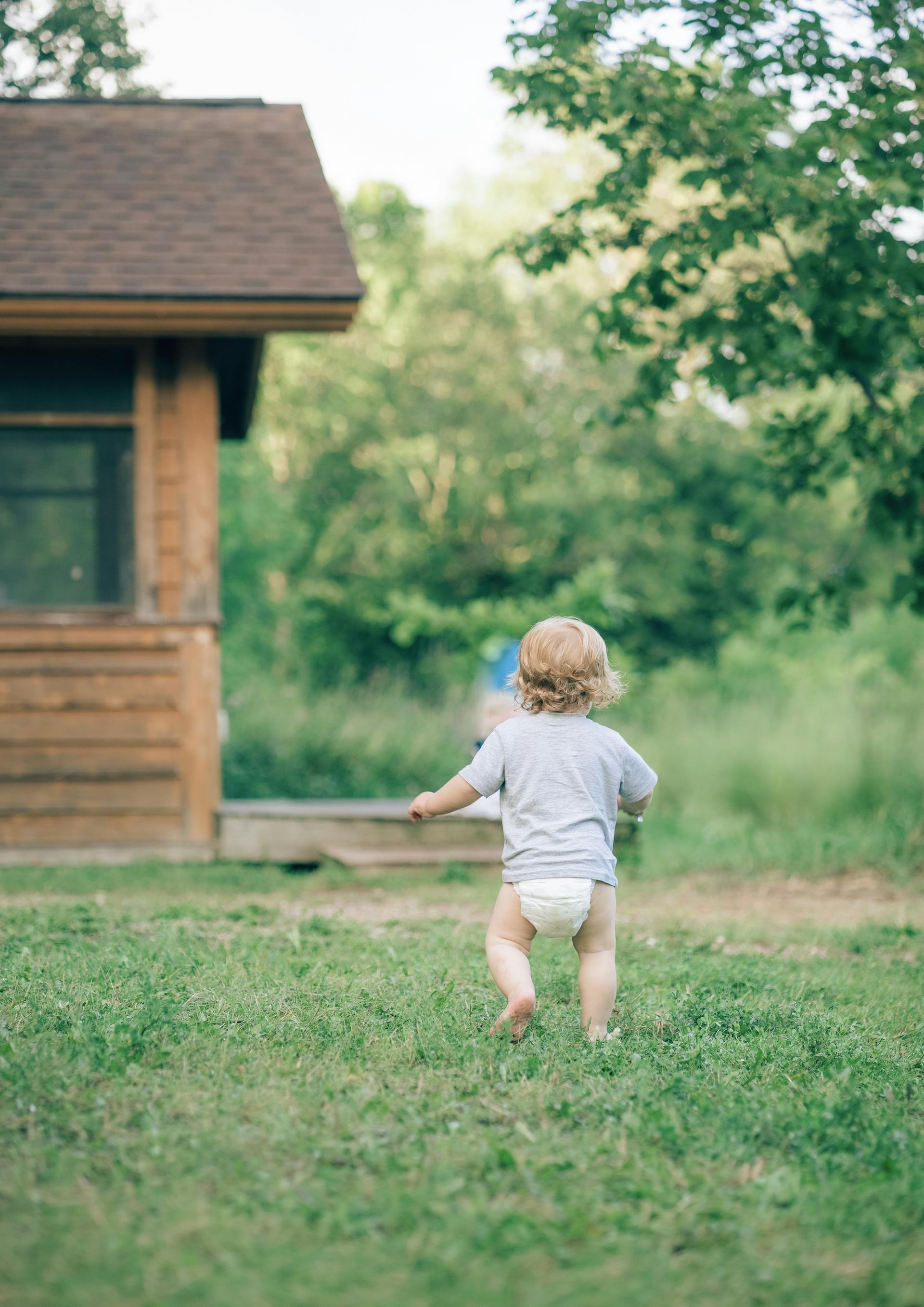 Vista trasera de un niño pequeño con pañal corriendo por el jardín | Fuente: Pexels