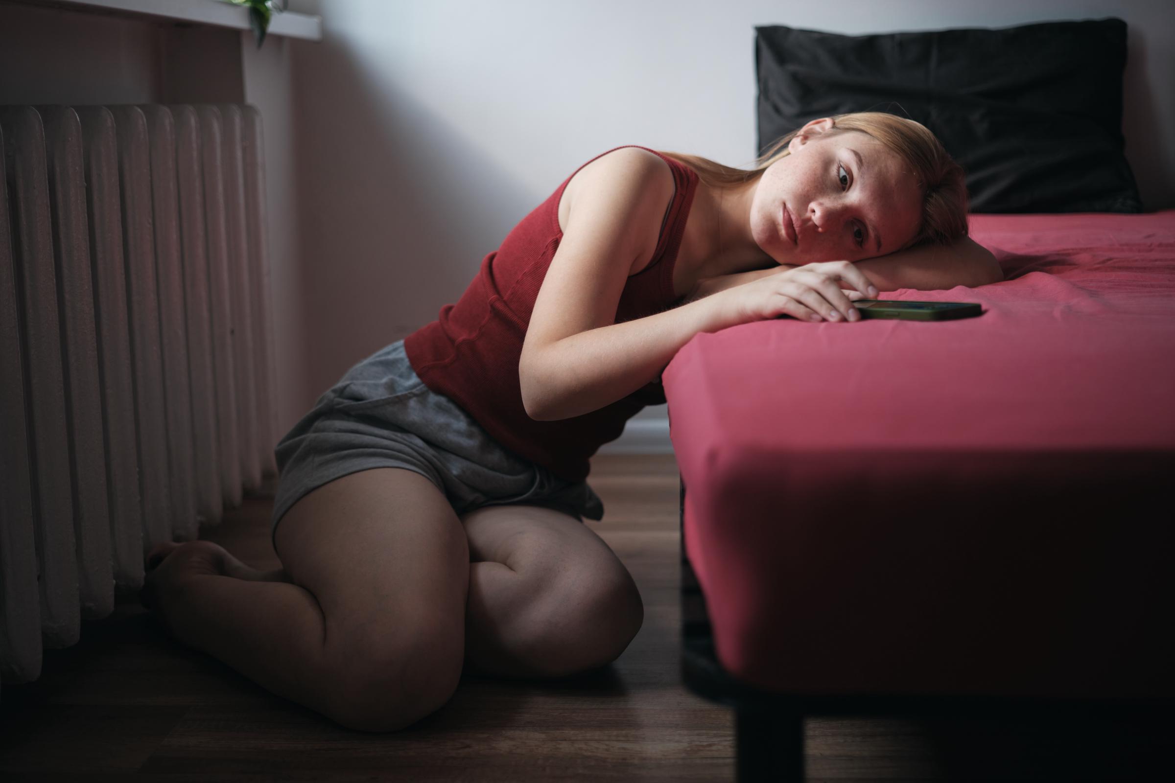 Una mujer de aspecto solemne sentada en el suelo a un lado de su cama | Fuente: Getty Images
