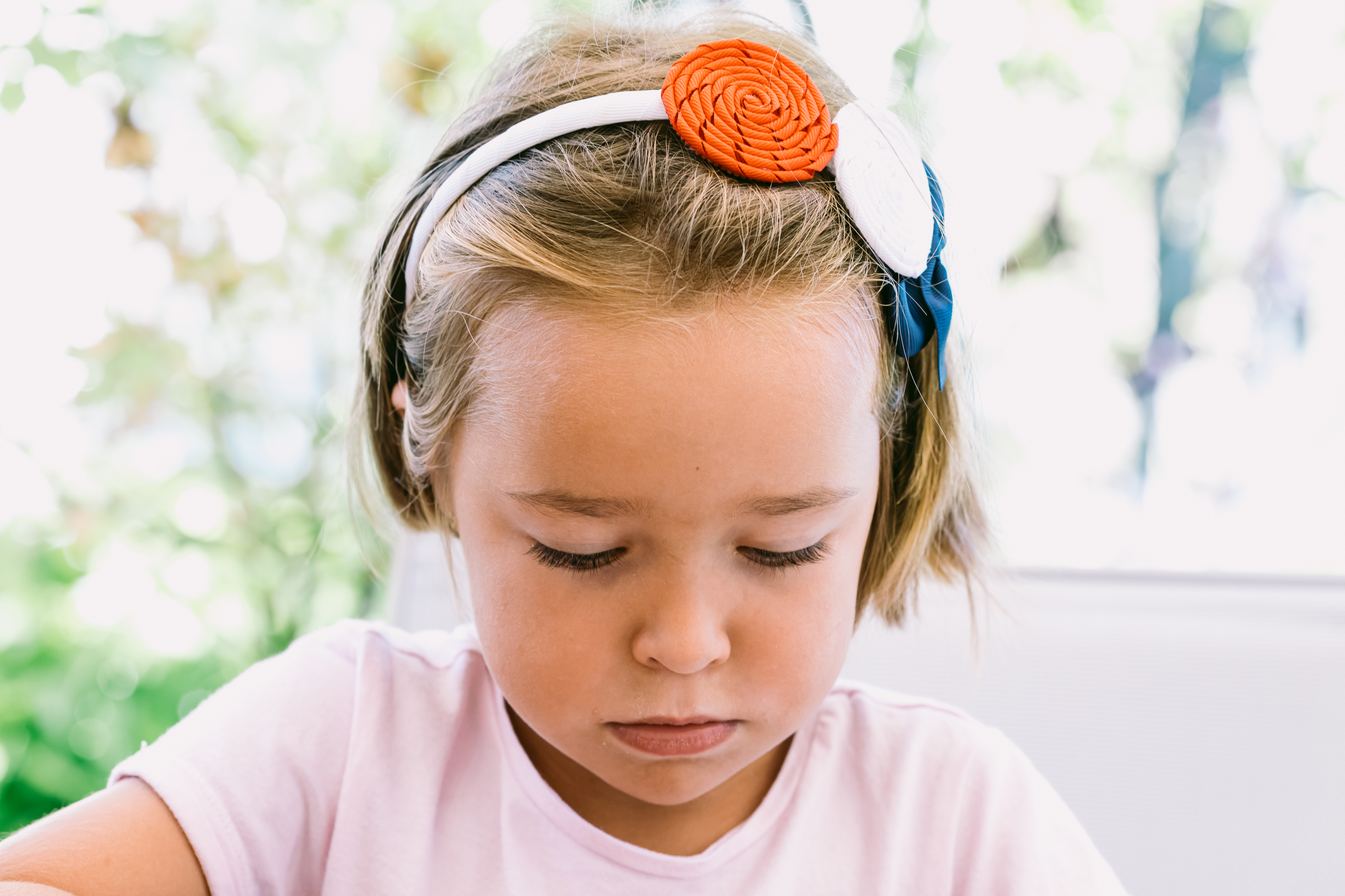 Retrato de una niña seria de pelo rubio, con una diadema blanca con adornos azules, rojos y blancos, con un jardín de fondo | Foto: Getty Images