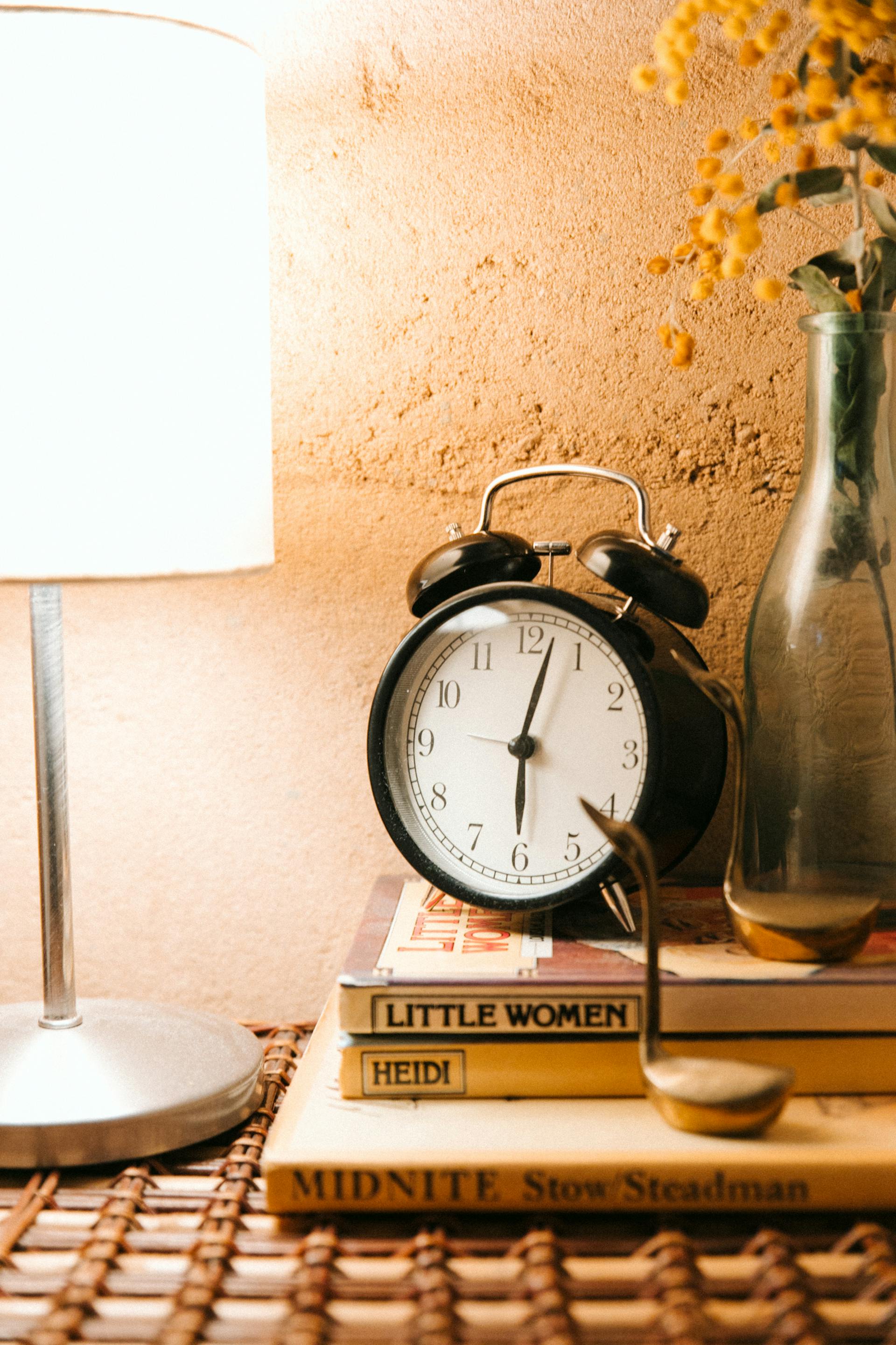 Un despertador vintage y una lámpara luminosa colocados en una mesilla de noche | Fuente: Pexels