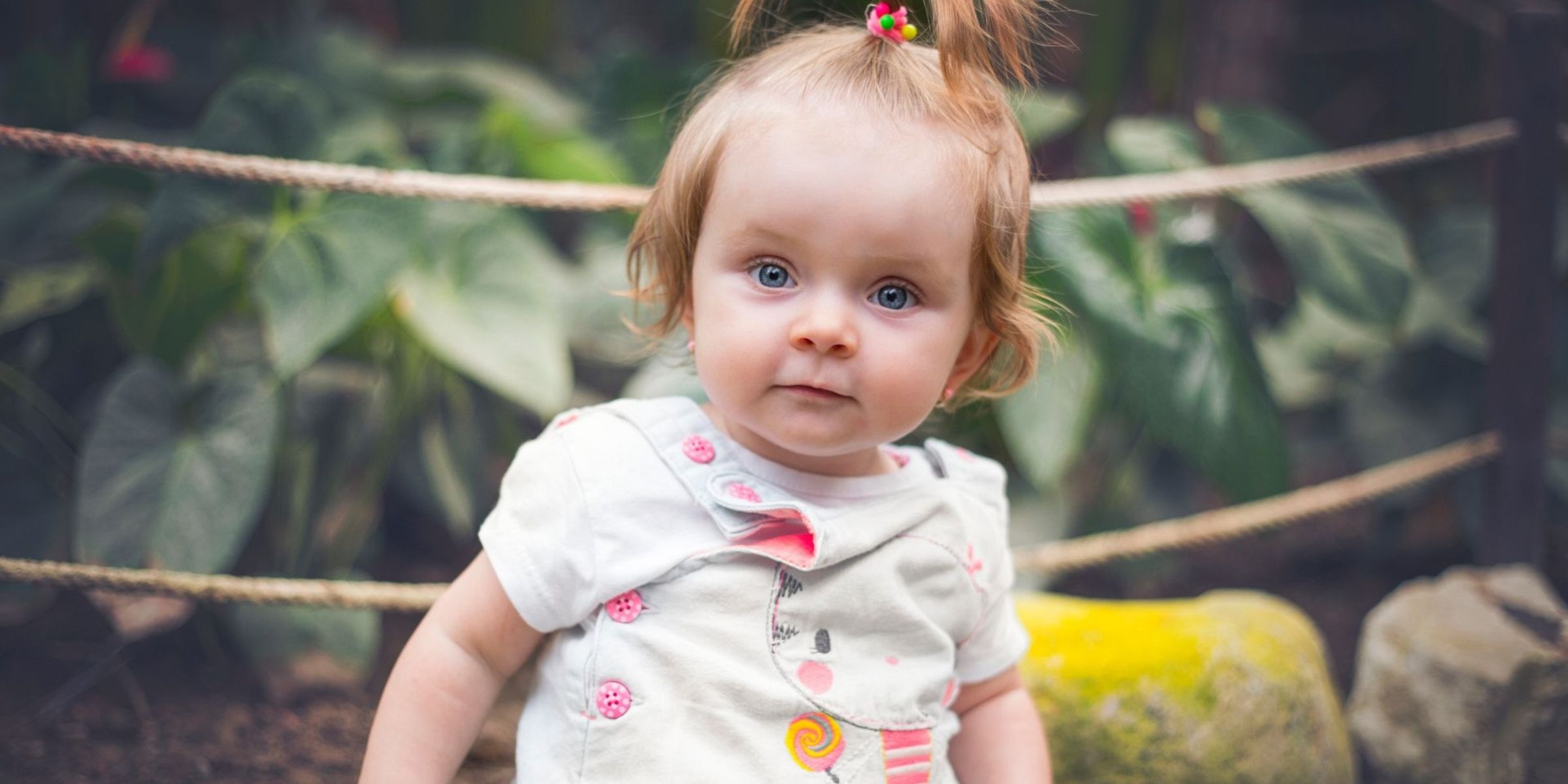 Niña con ojos azules y una pequeña coleta sentada al aire libre | Fuente: Pexels