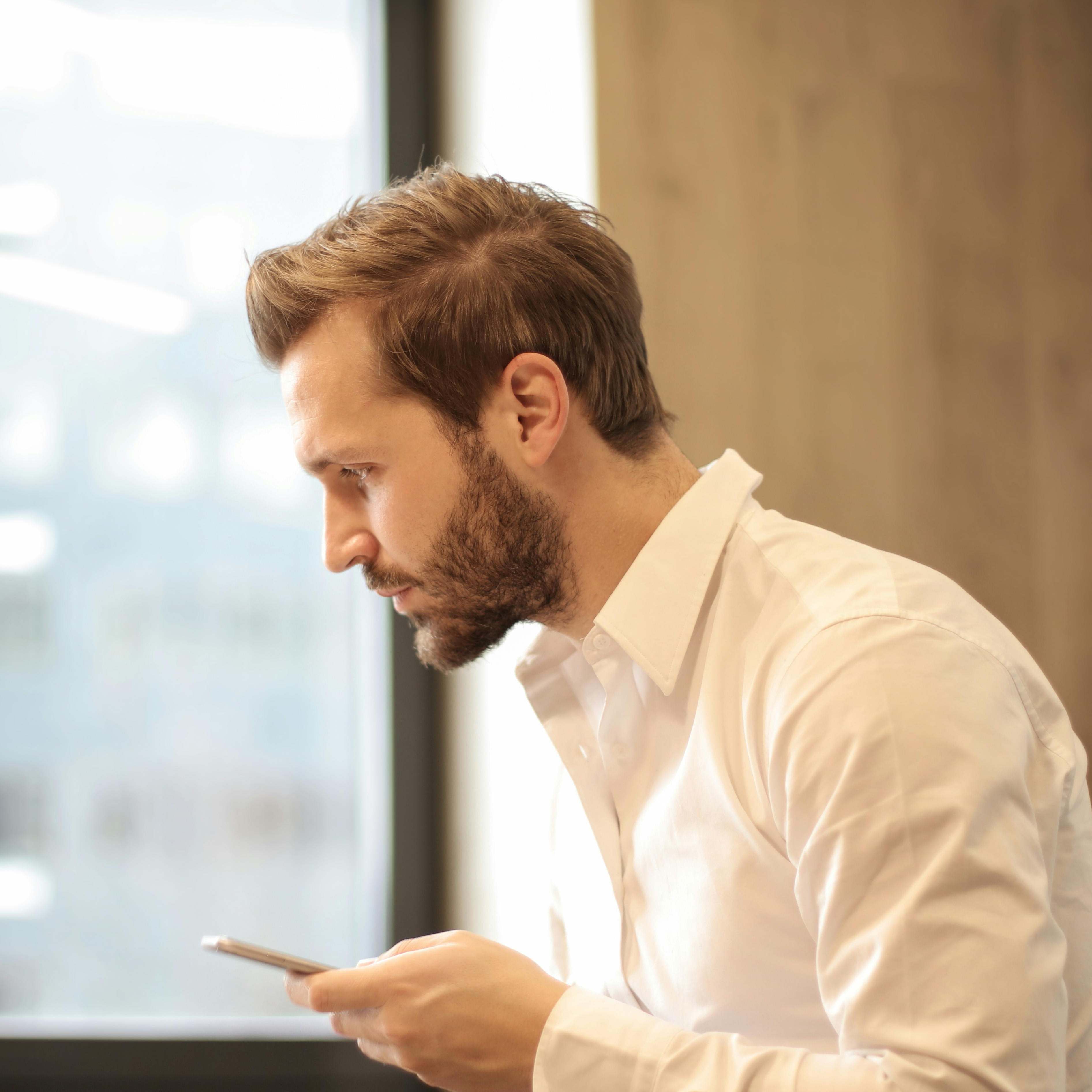 Un hombre con un teléfono en la mano, con aspecto contemplativo | Fuente: Pexels