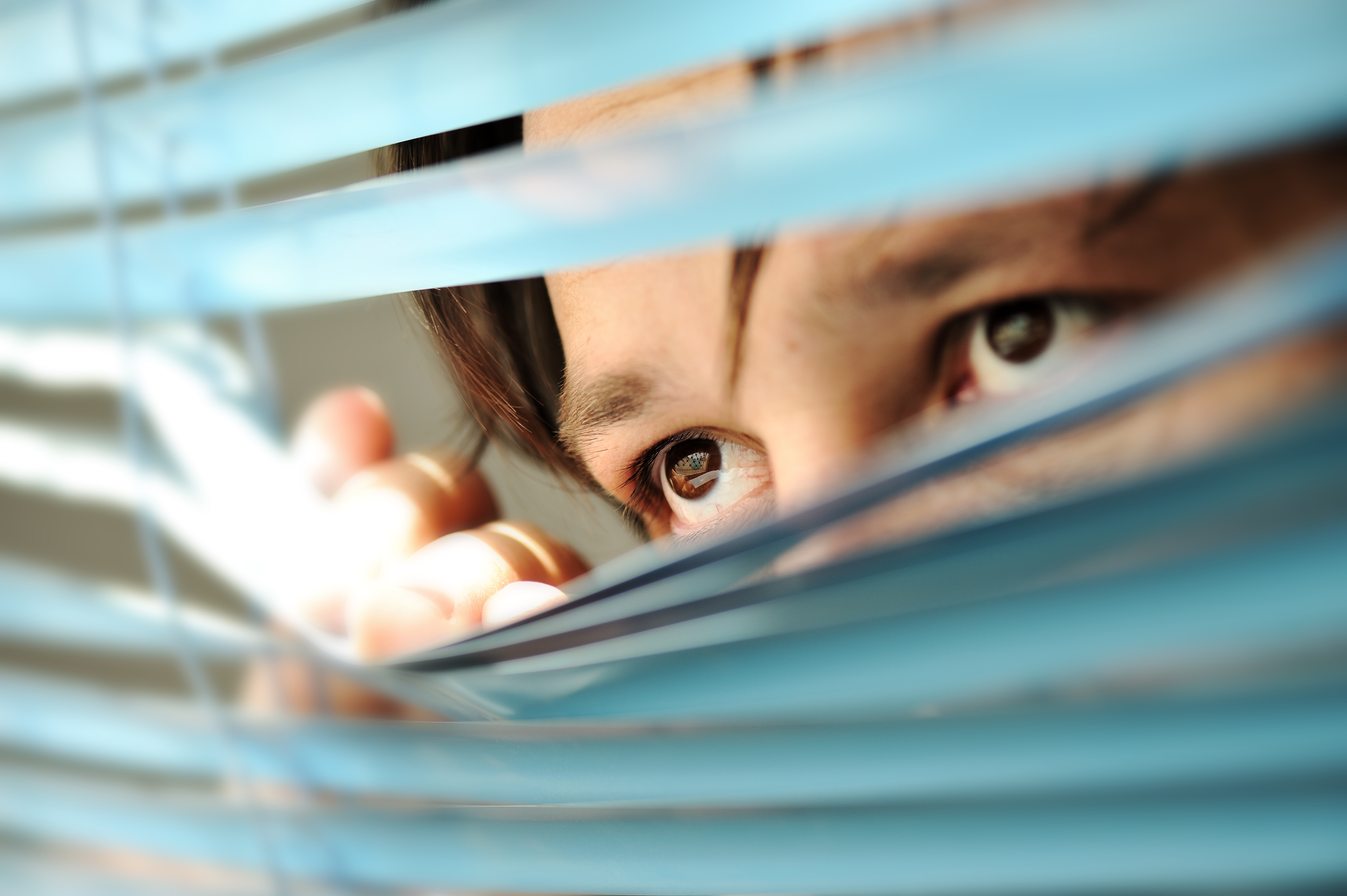 Hombre mirando a través de las persianas de la ventana. | Foto: Shutterstock