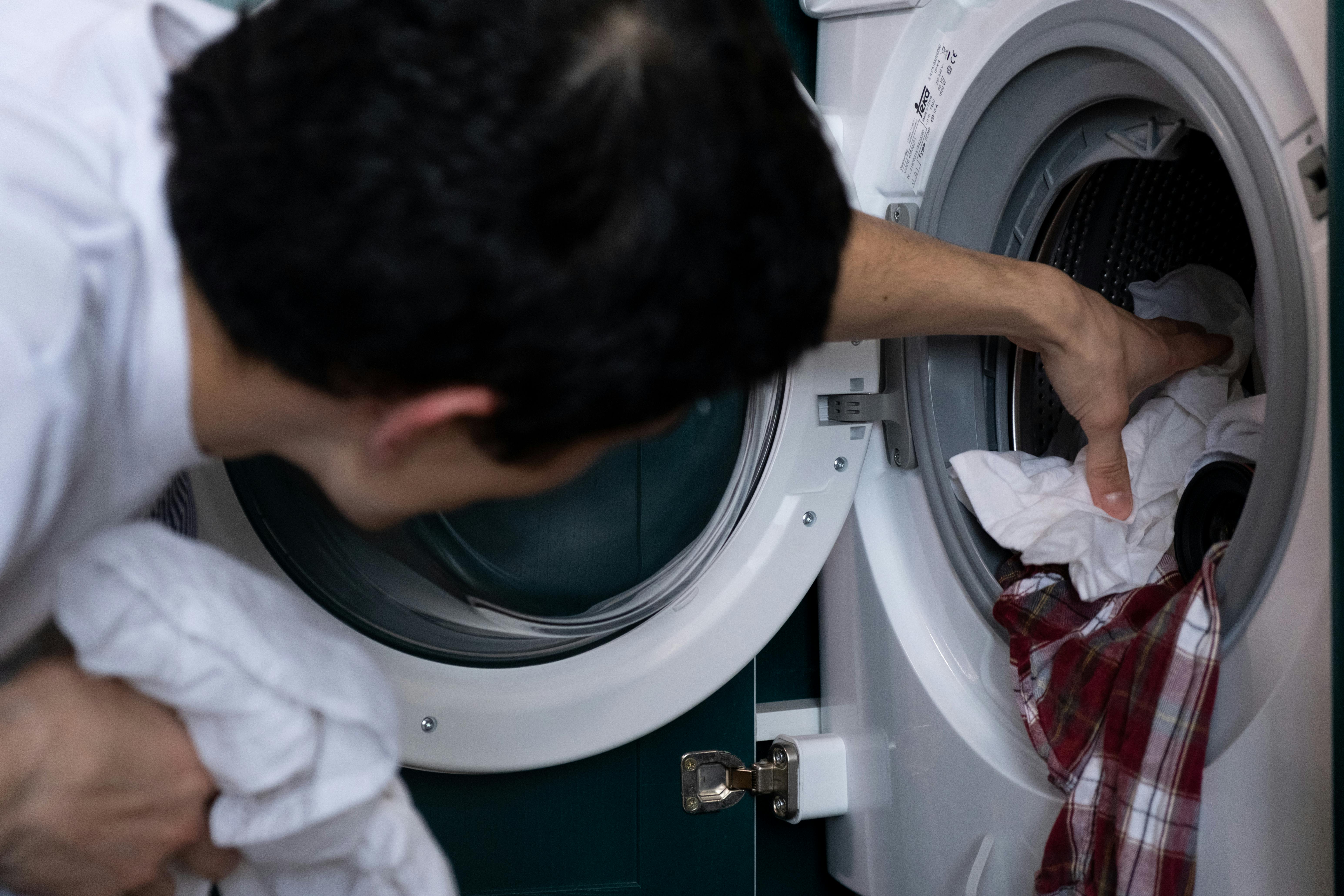 Un hombre metiendo ropa en una lavadora | Fuente: Pexels