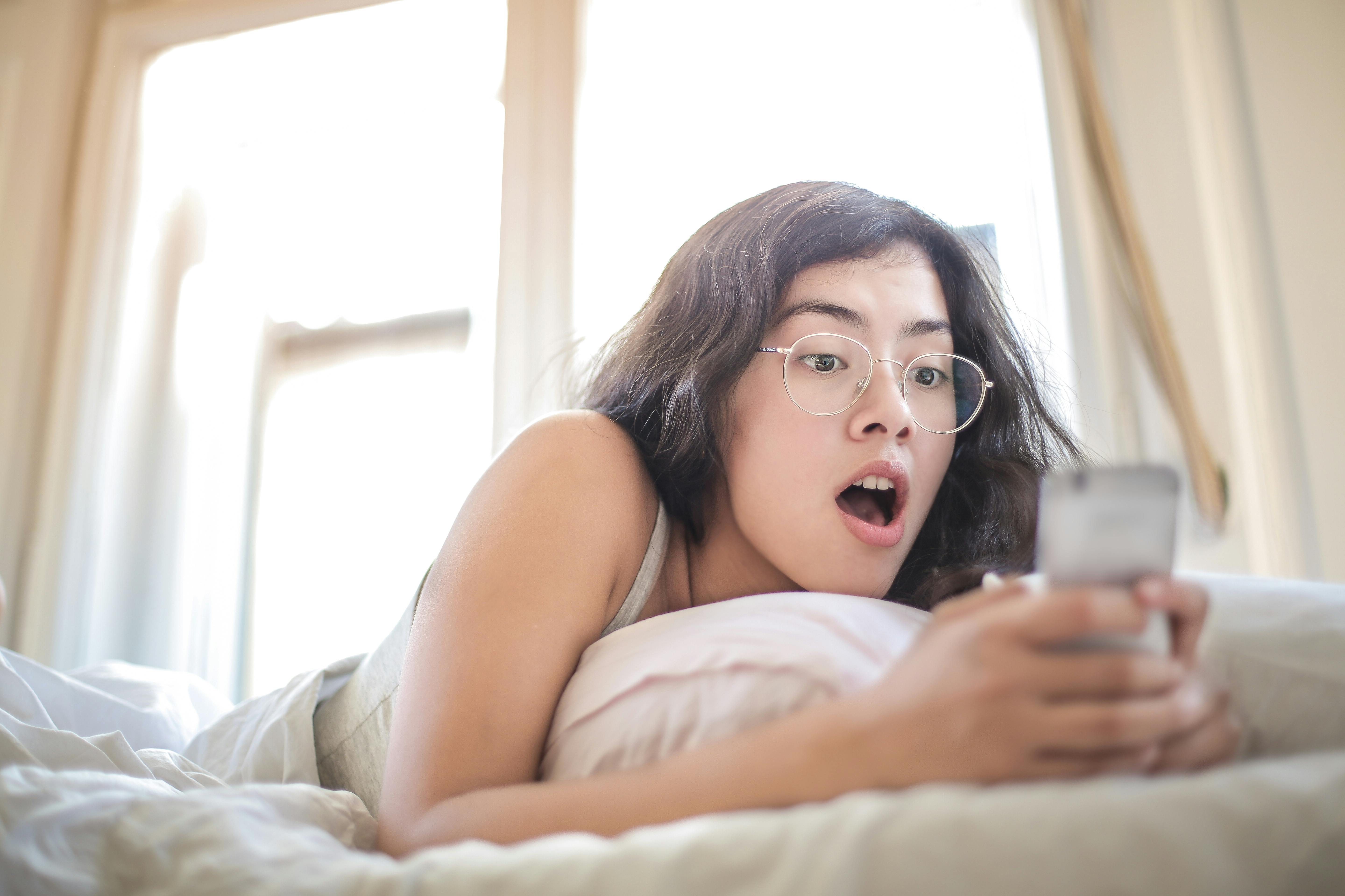 Una mujer tumbada en la cama mientras sostiene un smartphone | Fuente: Pexels