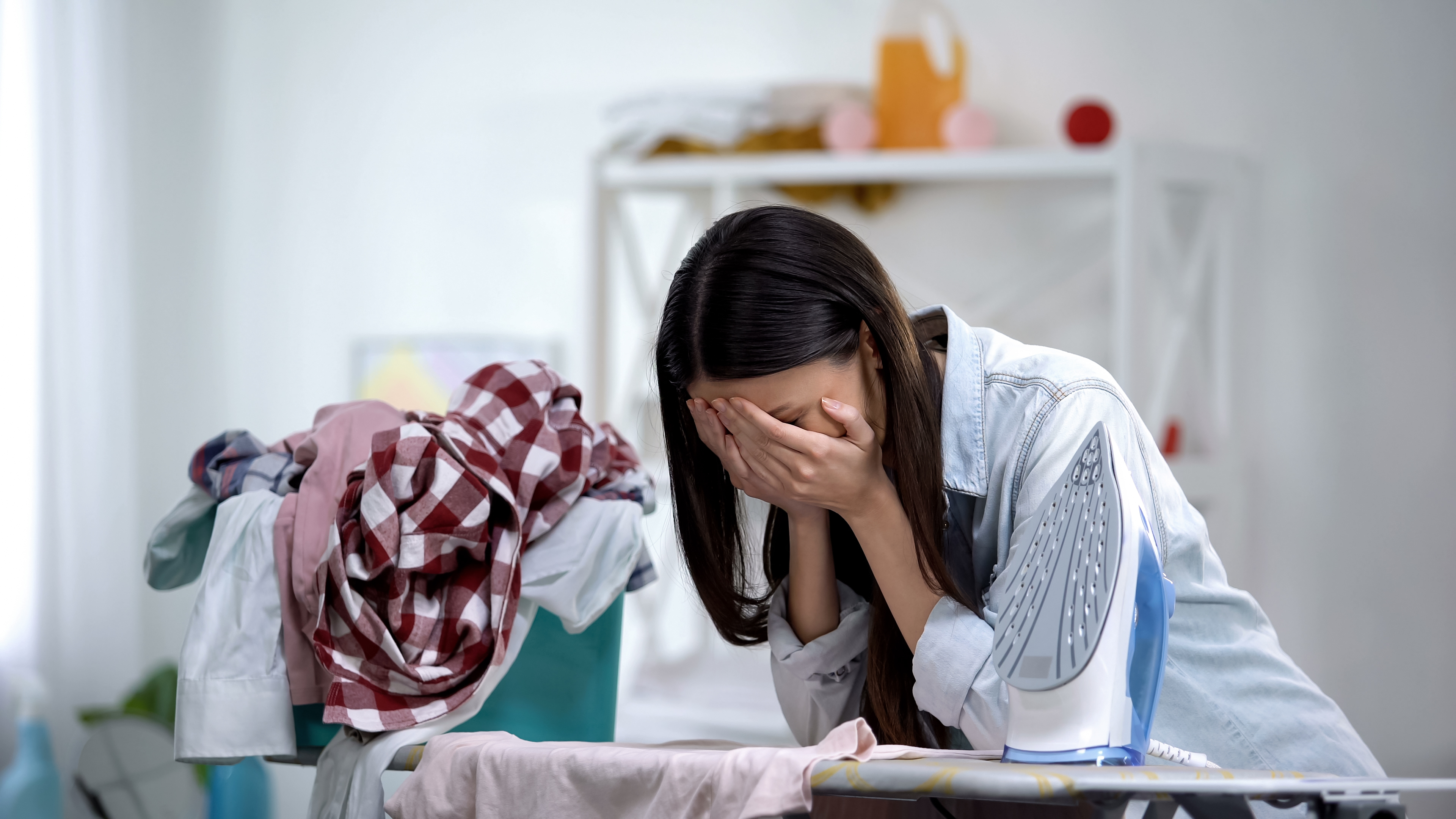 Una mujer estresada aparece llorando apoyada en la tabla de planchar. | Foto: Shutterstock