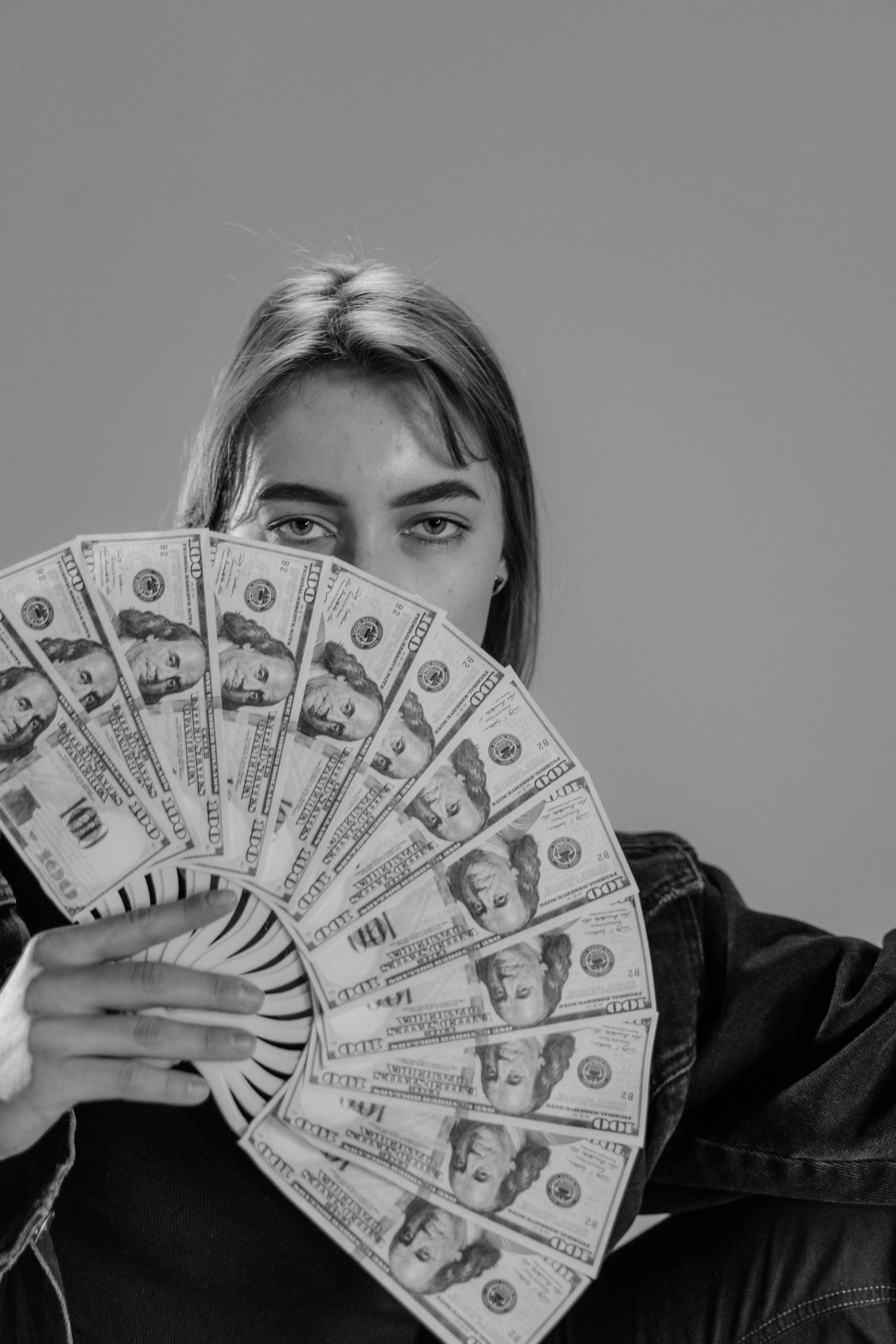 Una mujer sujetando billetes de 100$ como si fueran un abanico que le cubre parte de la cara | Foto: Pexels