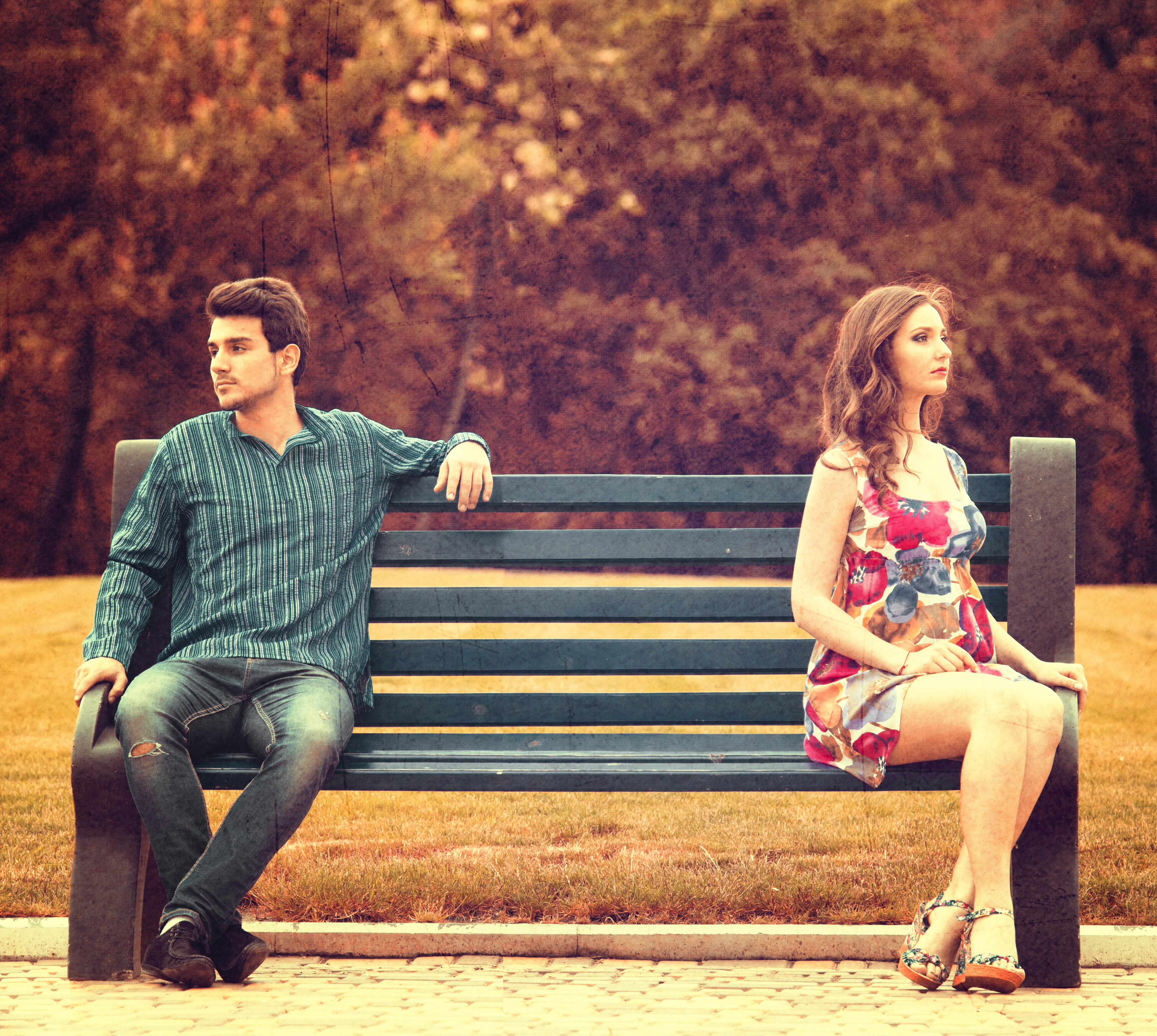 Una pareja joven sentada aparte en un banco de un parque. | Foto: Shutterstock
