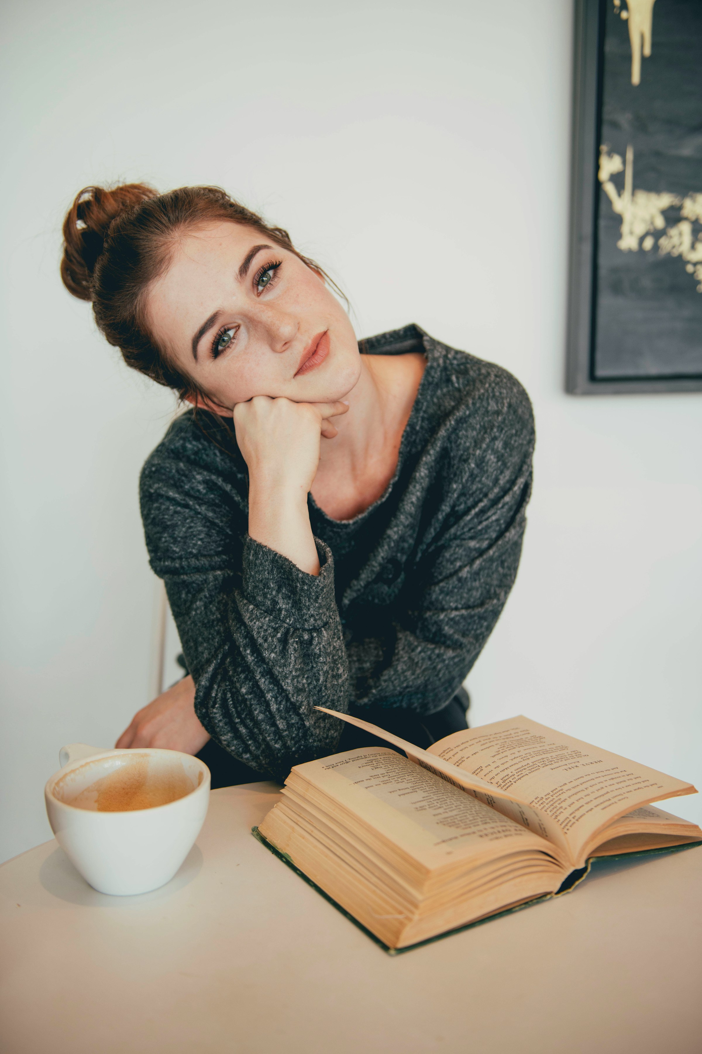 Una mujer sentada junto a una taza de café y un libro abierto | Fuente: Unsplash